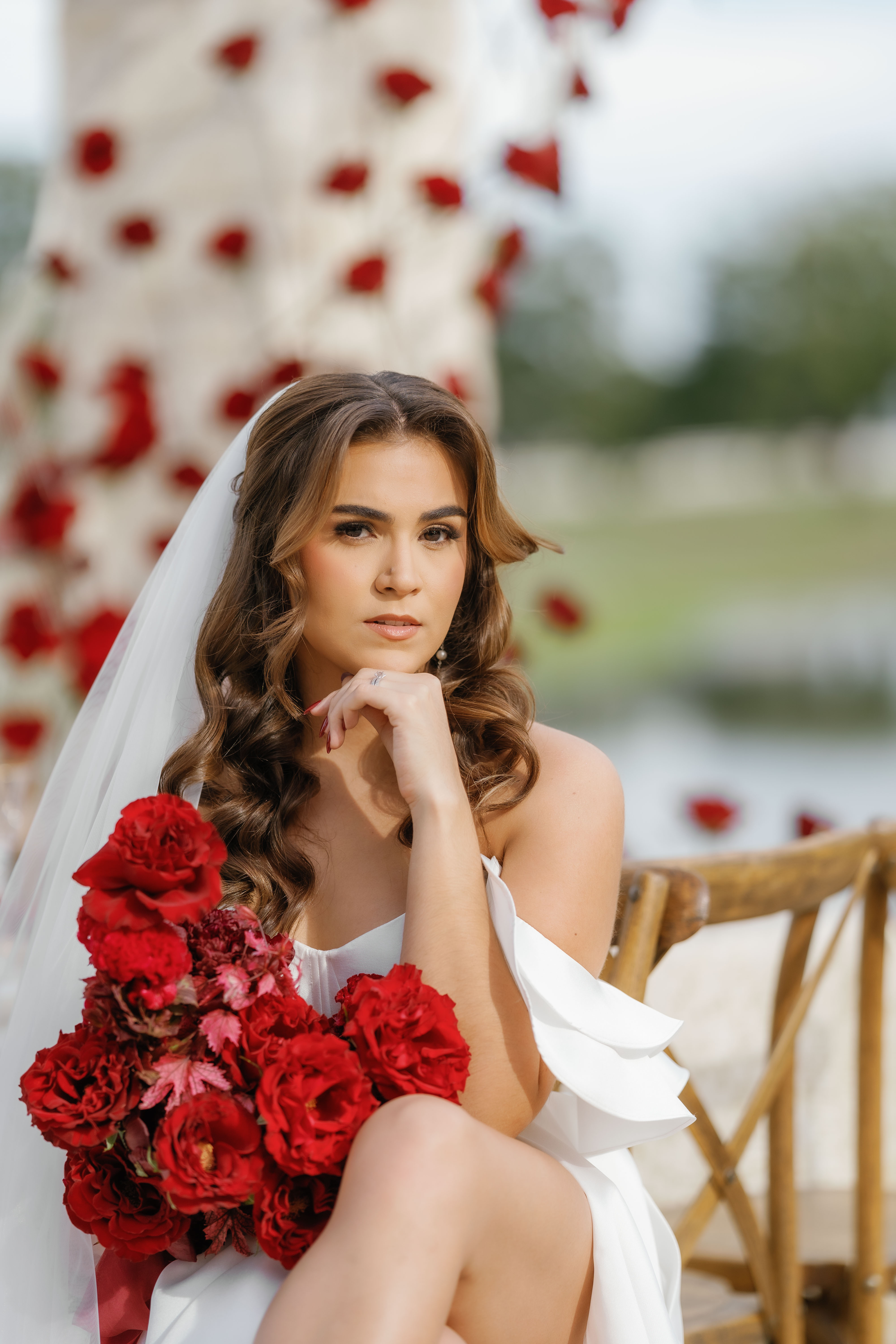 Bride in a white gown holding red roses in front of a soft floral installation.