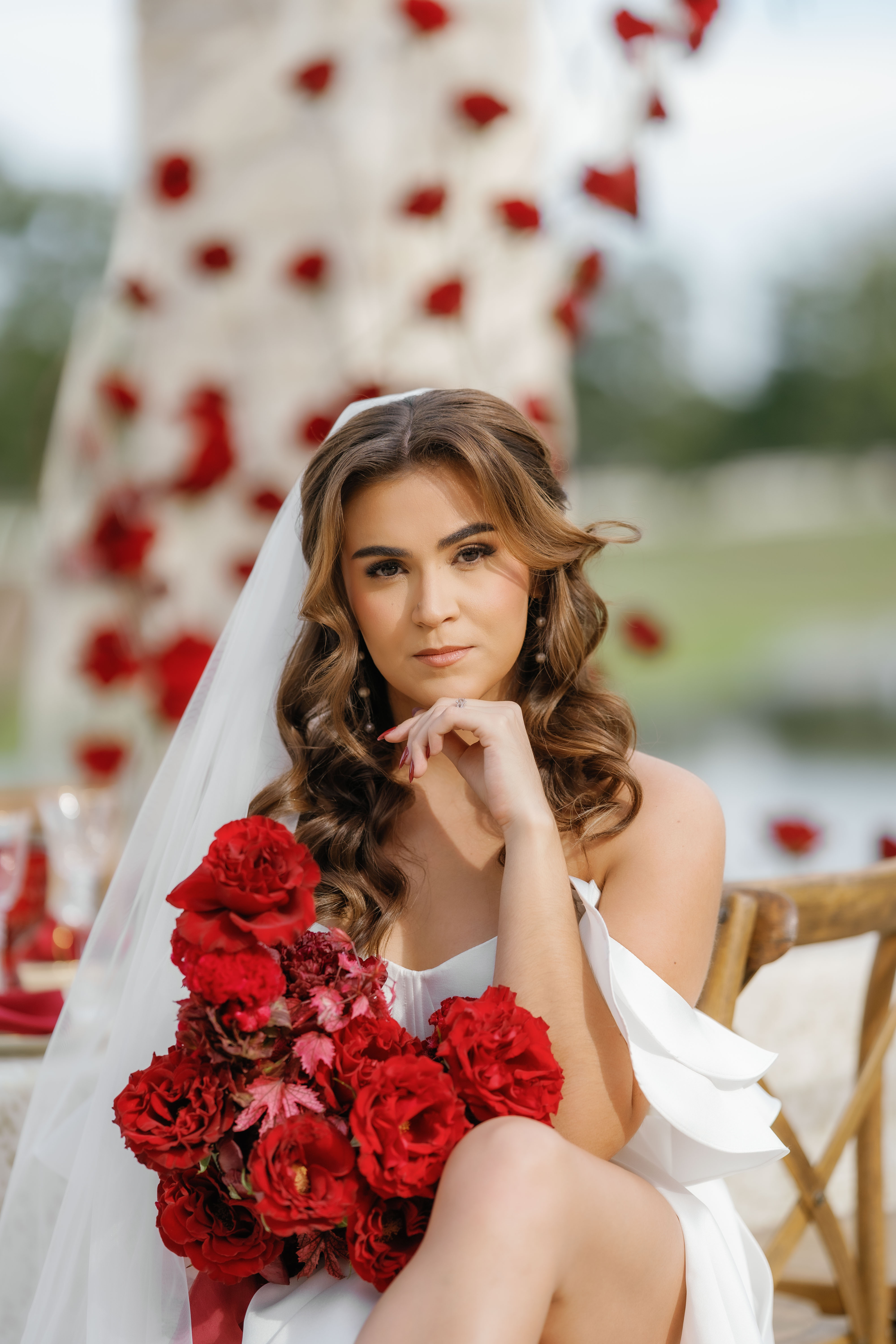 Bride in a white gown holding vibrant red roses before a floral installation backdrop.