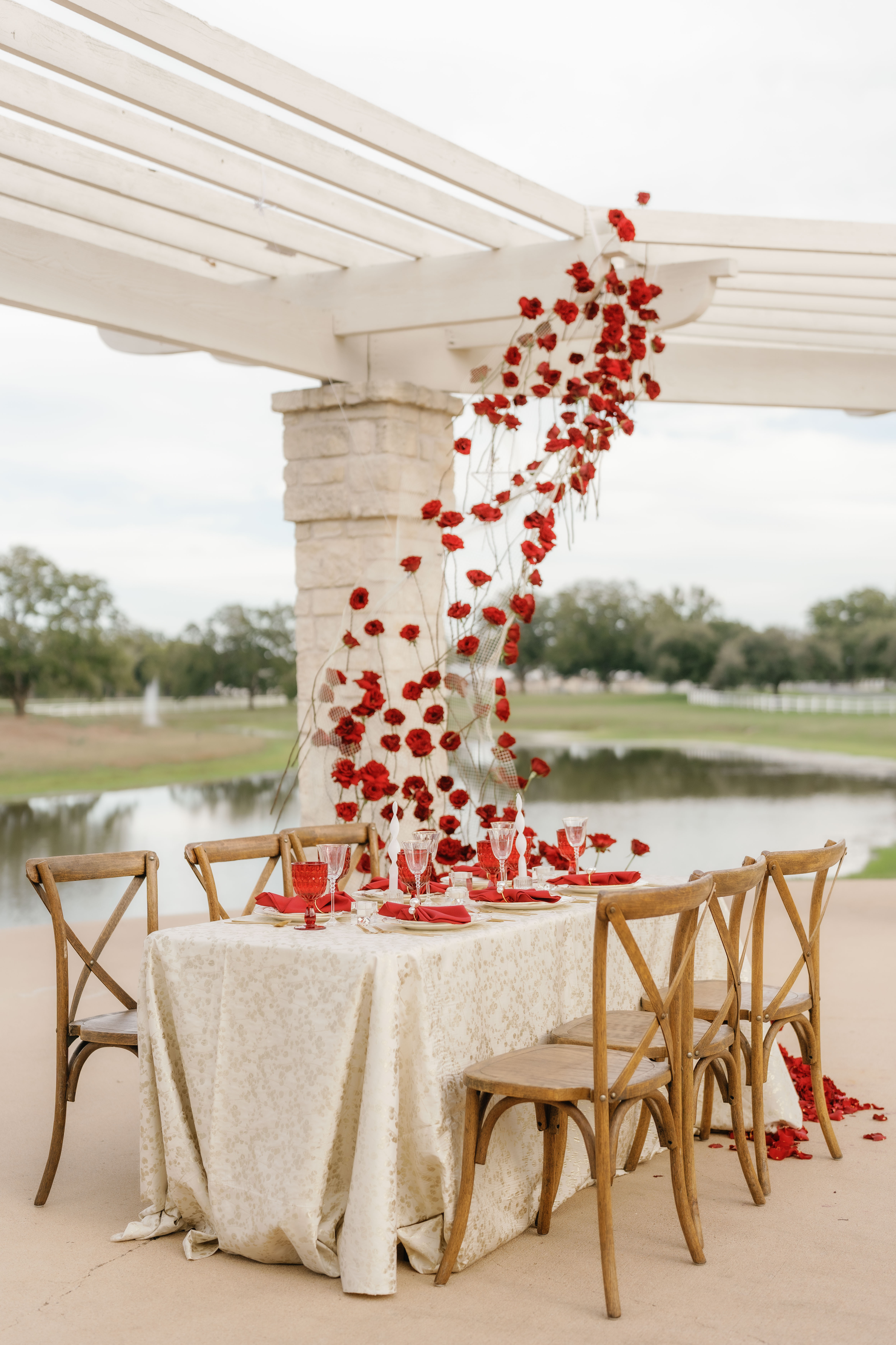 Red roses suspend in an airy sculptural installation above an outdoor dining table set with ruby glassware and textured ivory linens.