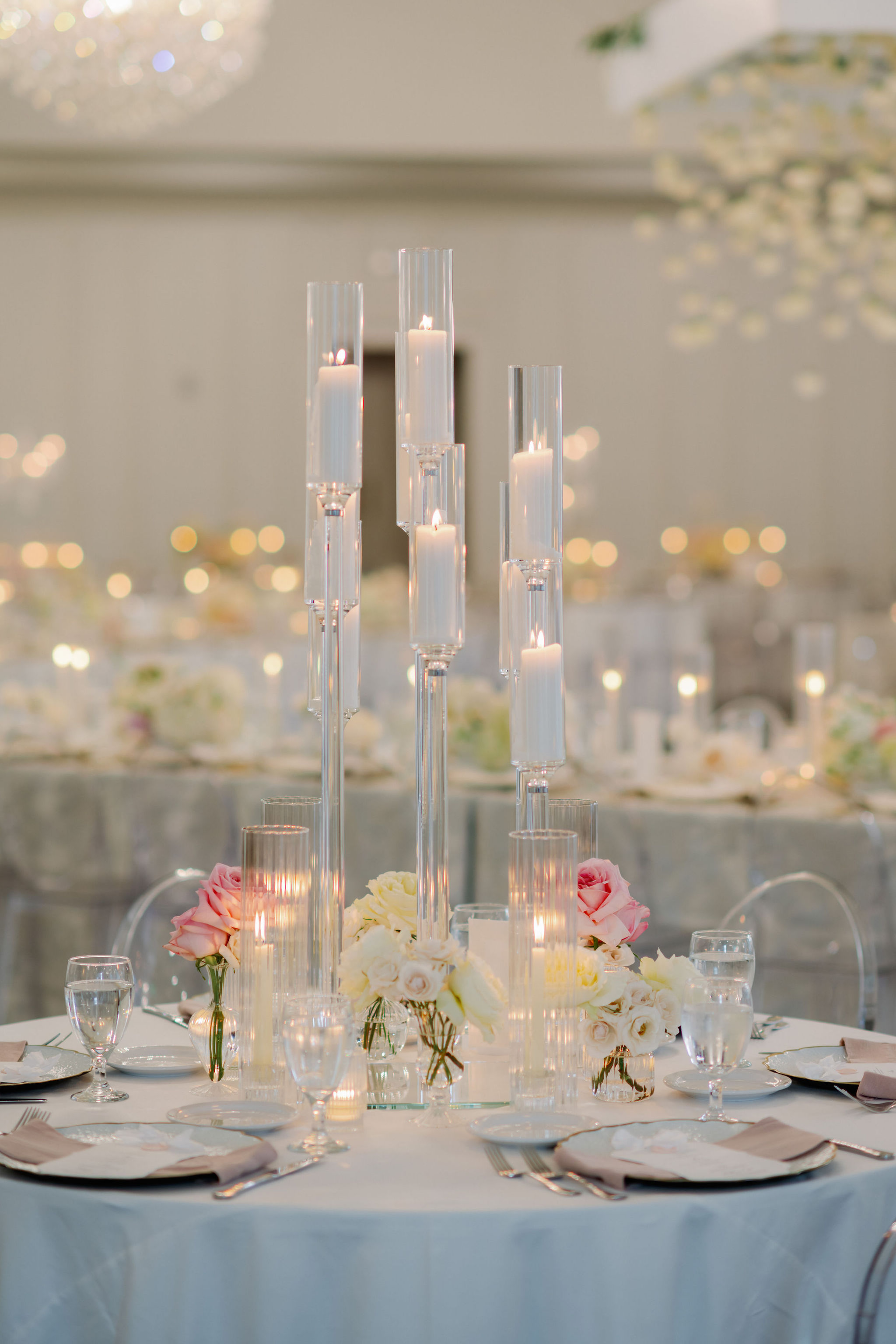 Tall glass candelabras with glowing white candles illuminate a wedding reception table adorned with blush and ivory roses.