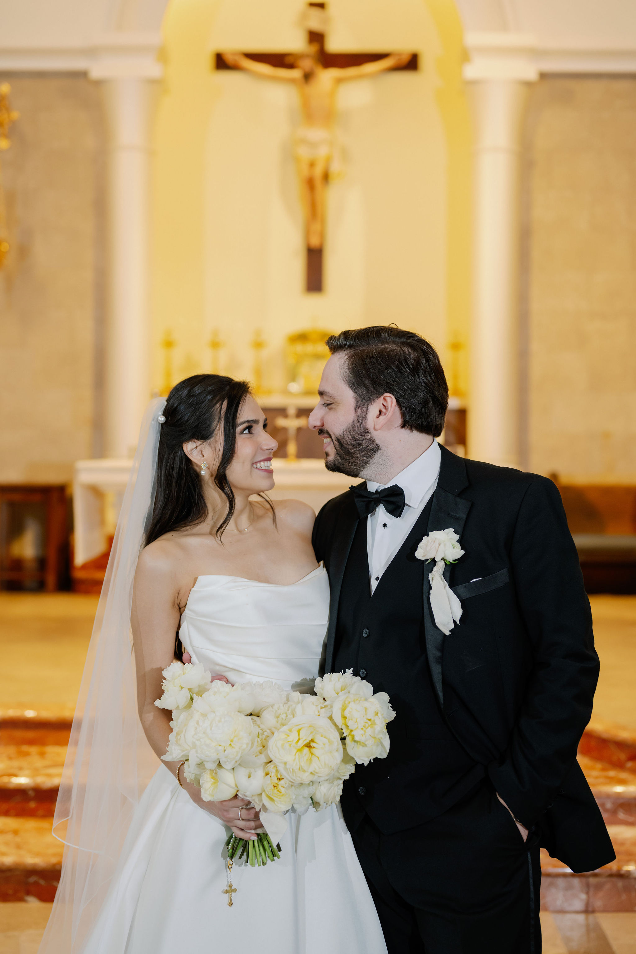 Bride holding a white peony and rose bouquet smiling with the groom inside a church.