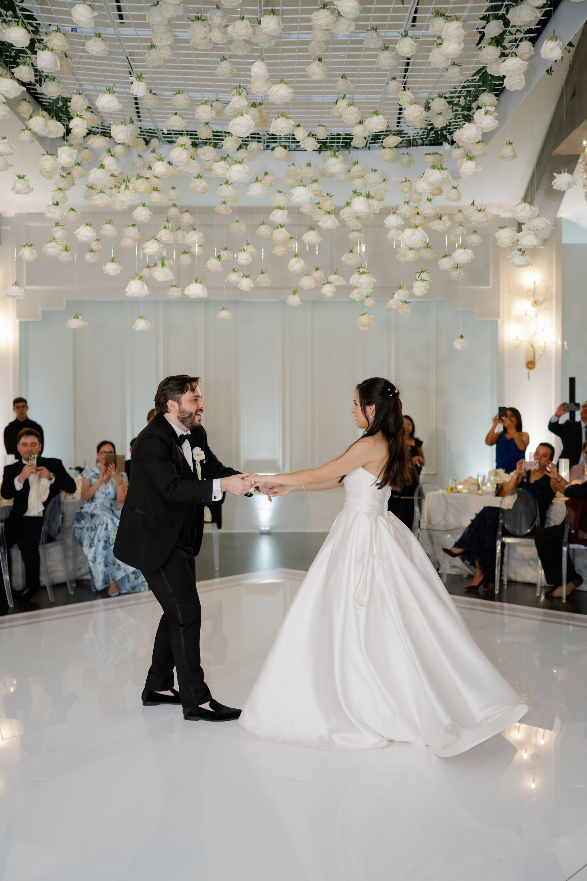 A bride and groom share a dance beneath a suspended ceiling installation of white roses.
