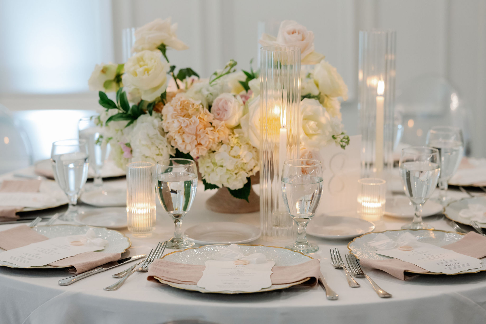 A romantic wedding tablescape featuring blush and white floral arrangements, fluted glass candleholders, and elegant place settings.