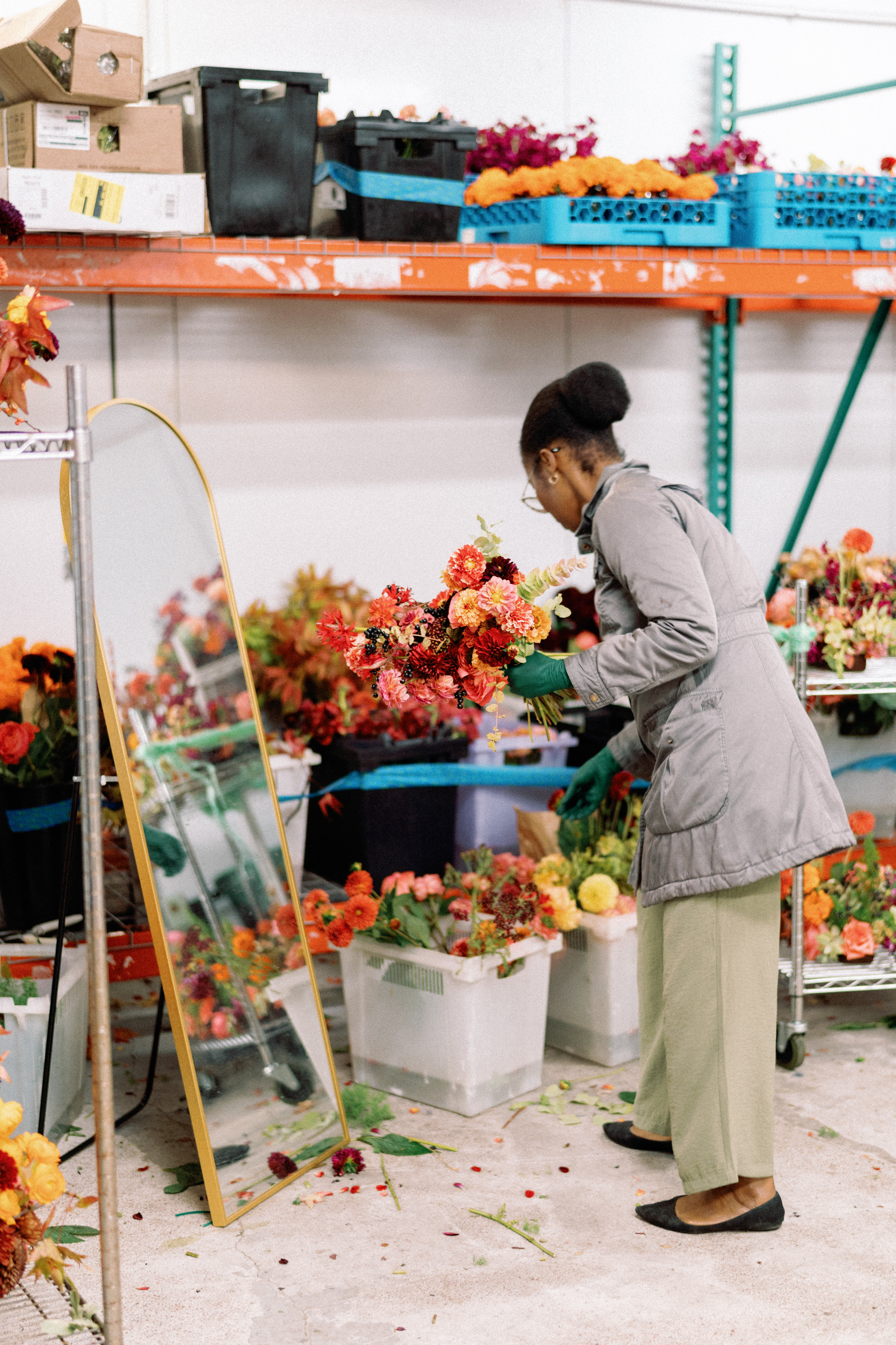 A floral designer crafts a vibrant bouquet of peach, coral, and deep red dahlias in a studio setting.