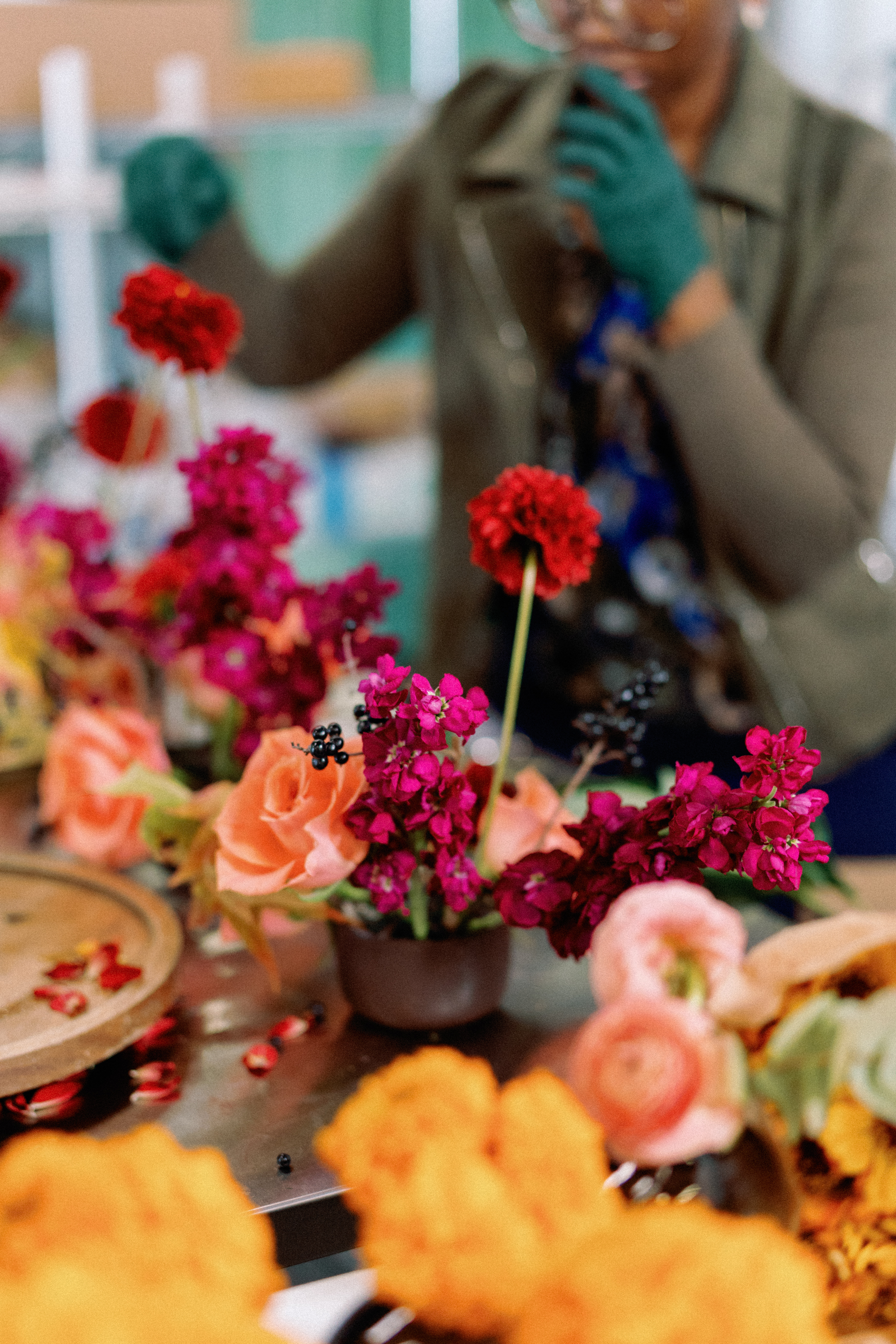 Vibrant floral arrangement featuring magenta blossoms, peach roses, and a red stem with a florist working in the blurred background.