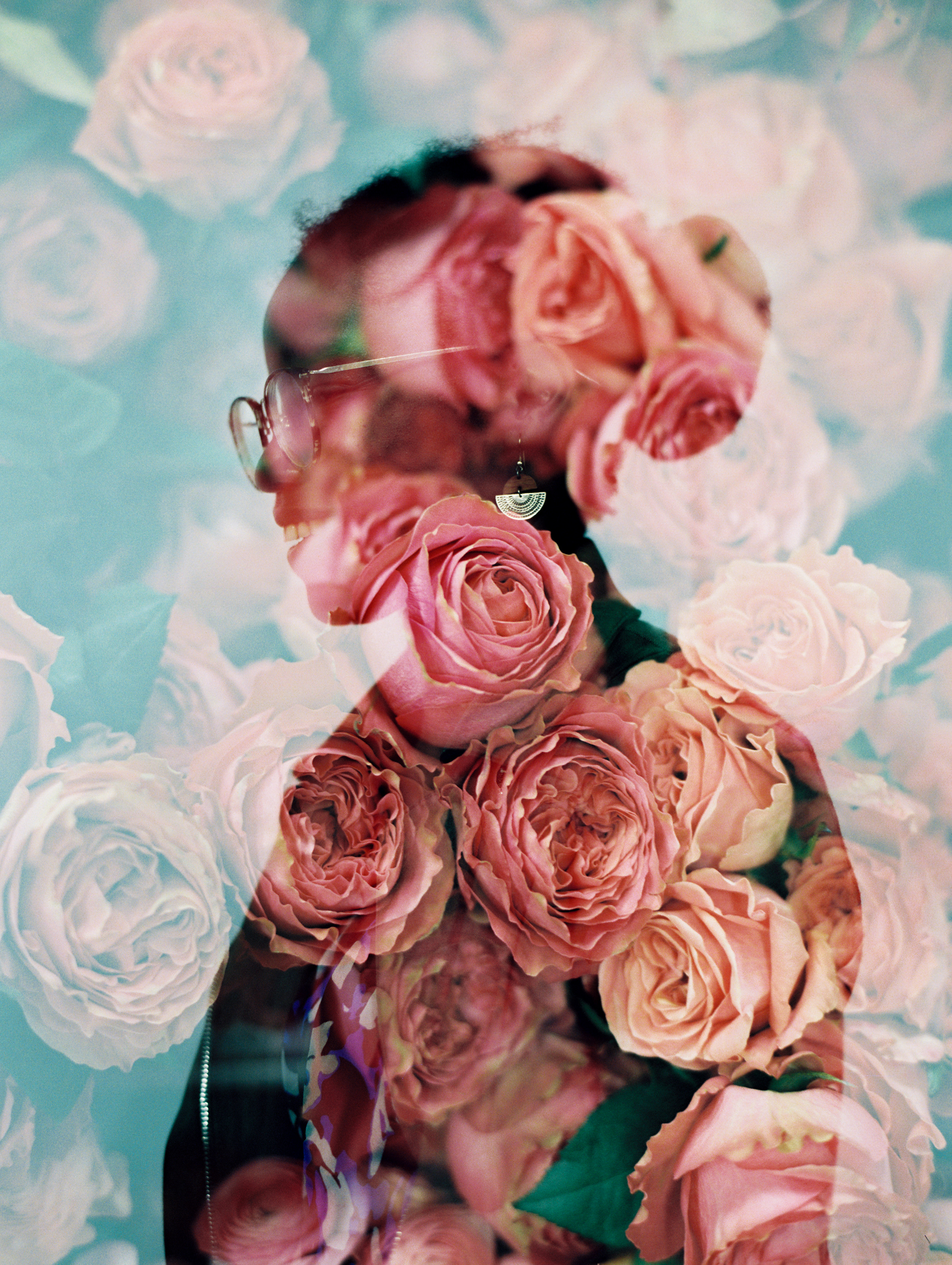 Double-exposure portrait blending a smiling person wearing glasses with lush pink and peach garden roses.
