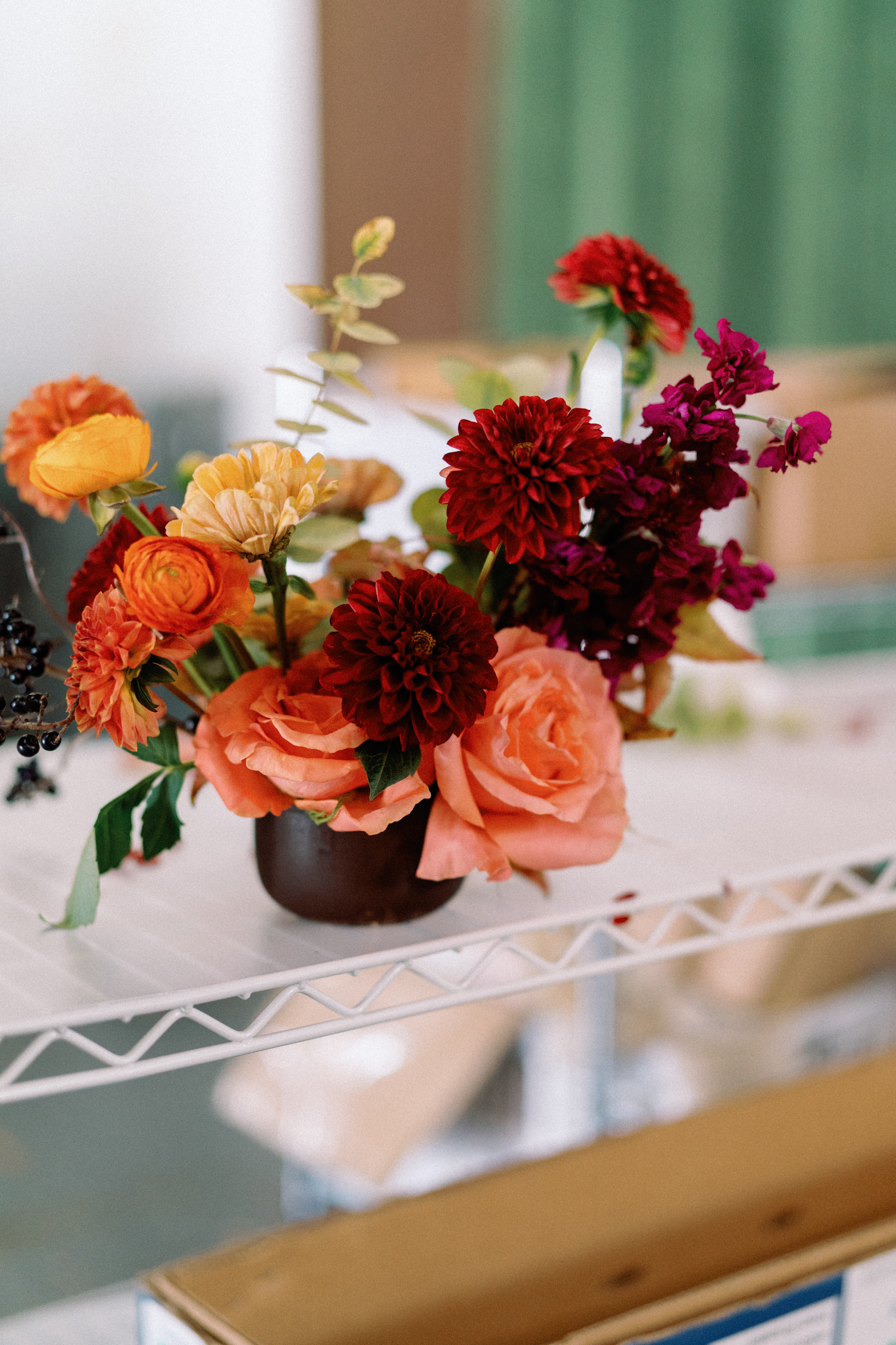 Deep red dahlias and peach roses arranged with delicate greenery on a white wire shelf.