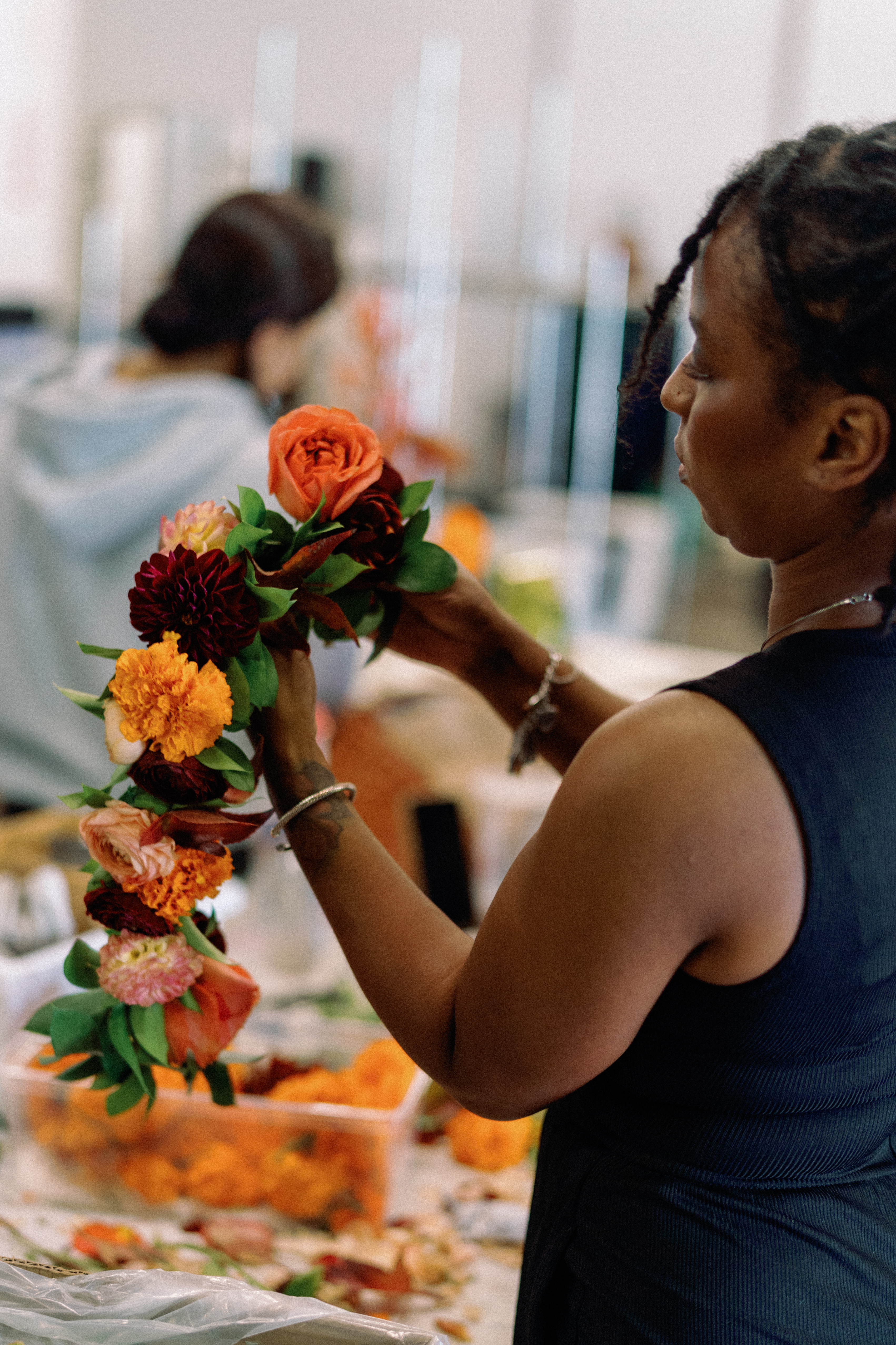 A florist arranges vibrant peach and deep red roses by hand in a bright workshop setting.