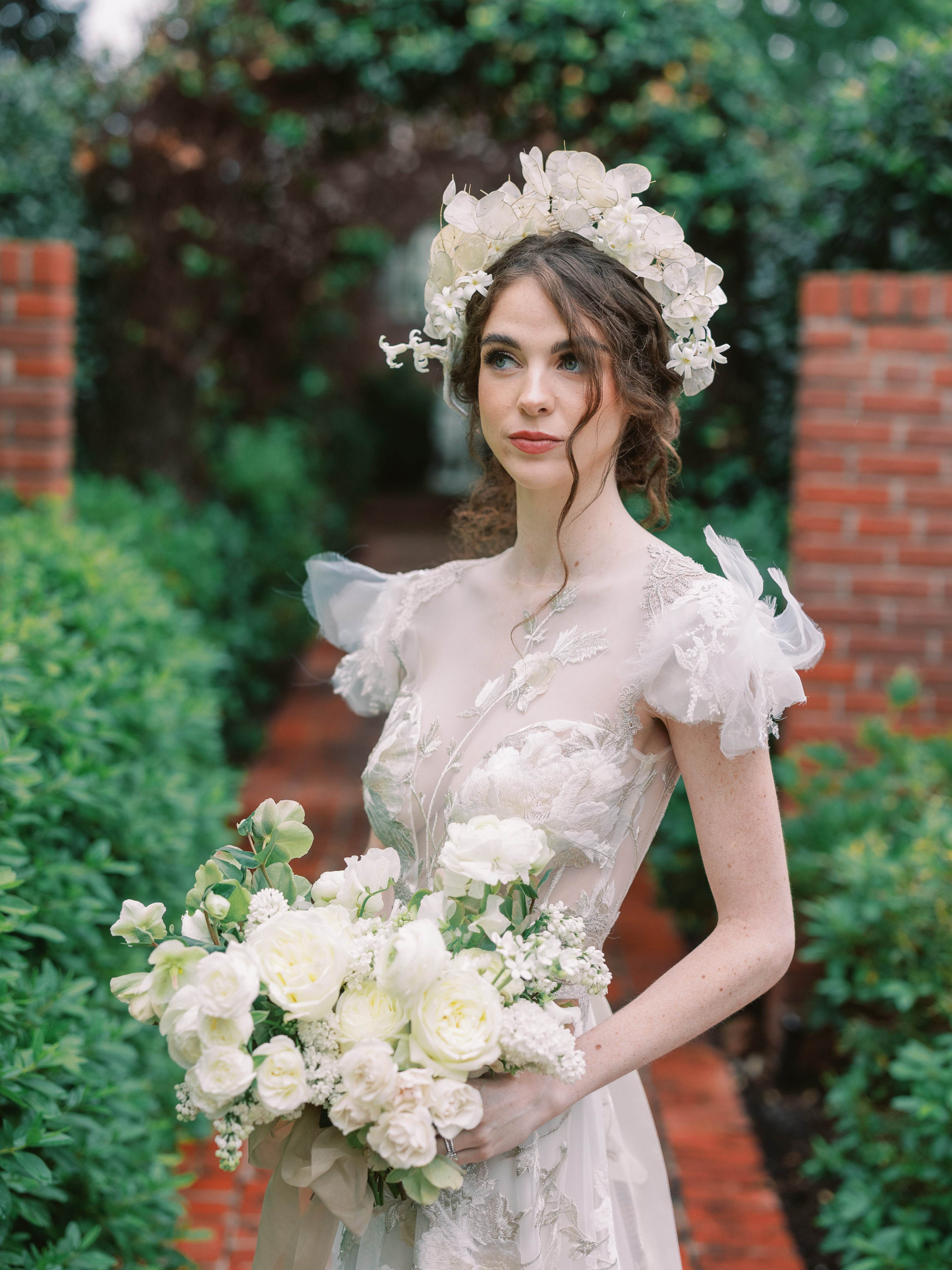 A bride wearing a delicate floral crown of lunaria and white blossoms holds an all-white bridal bouquet.