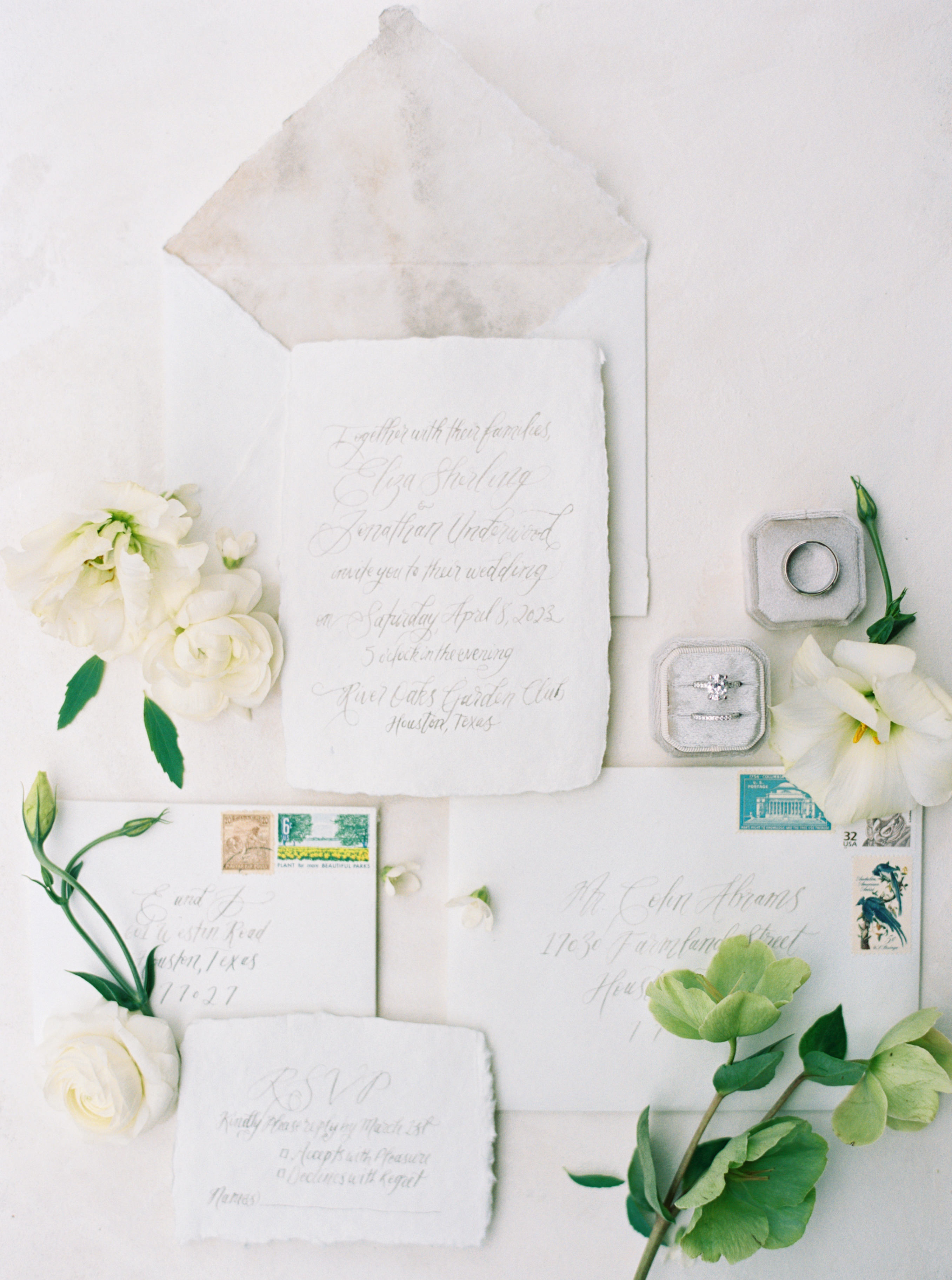 Calligraphy wedding invitation suite on handmade paper styled with delicate white flowers and a velvet ring box.