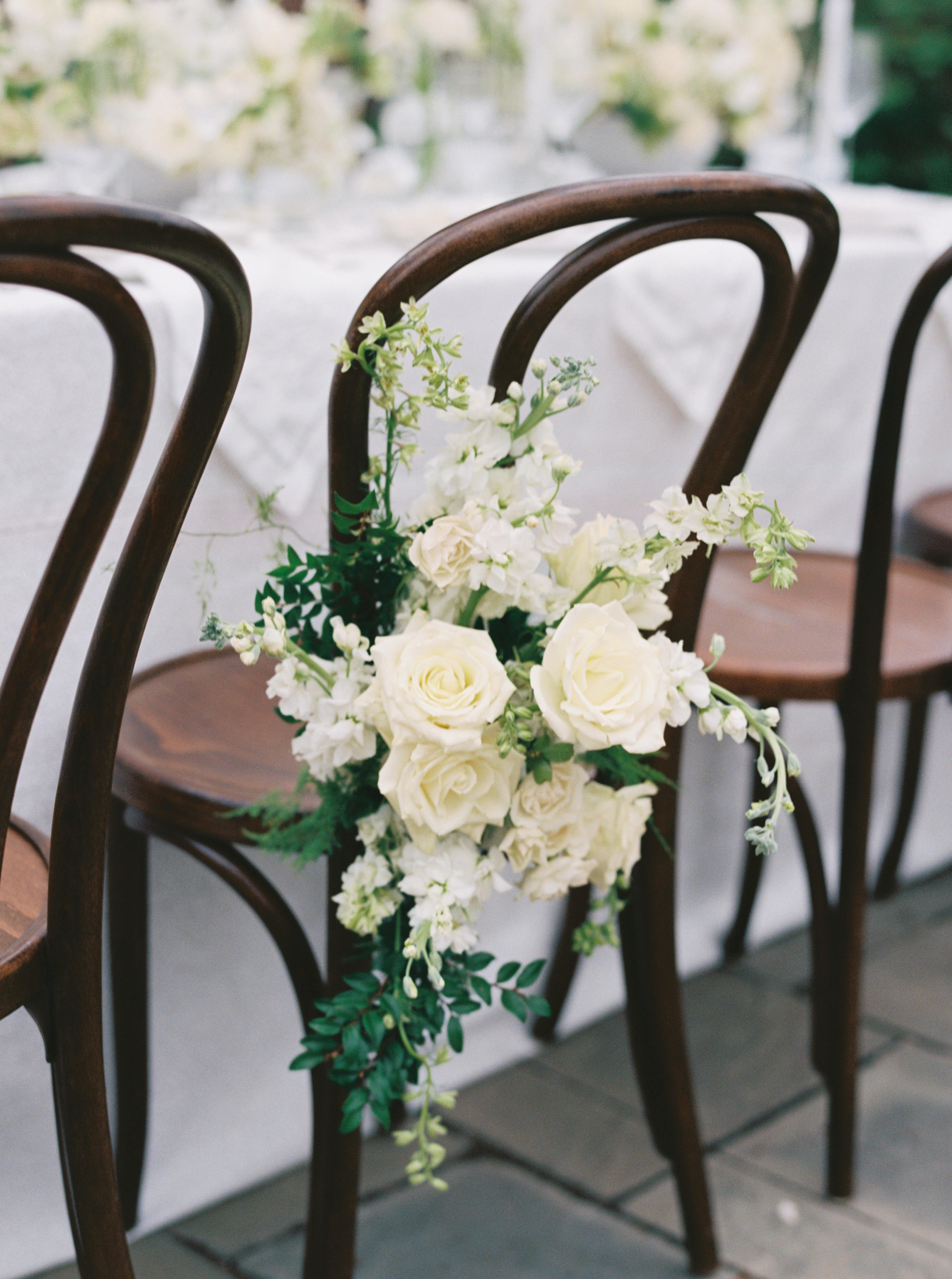 Cream and white roses paired with delicate white blossoms and greenery adorn a dark wooden bentwood chair.