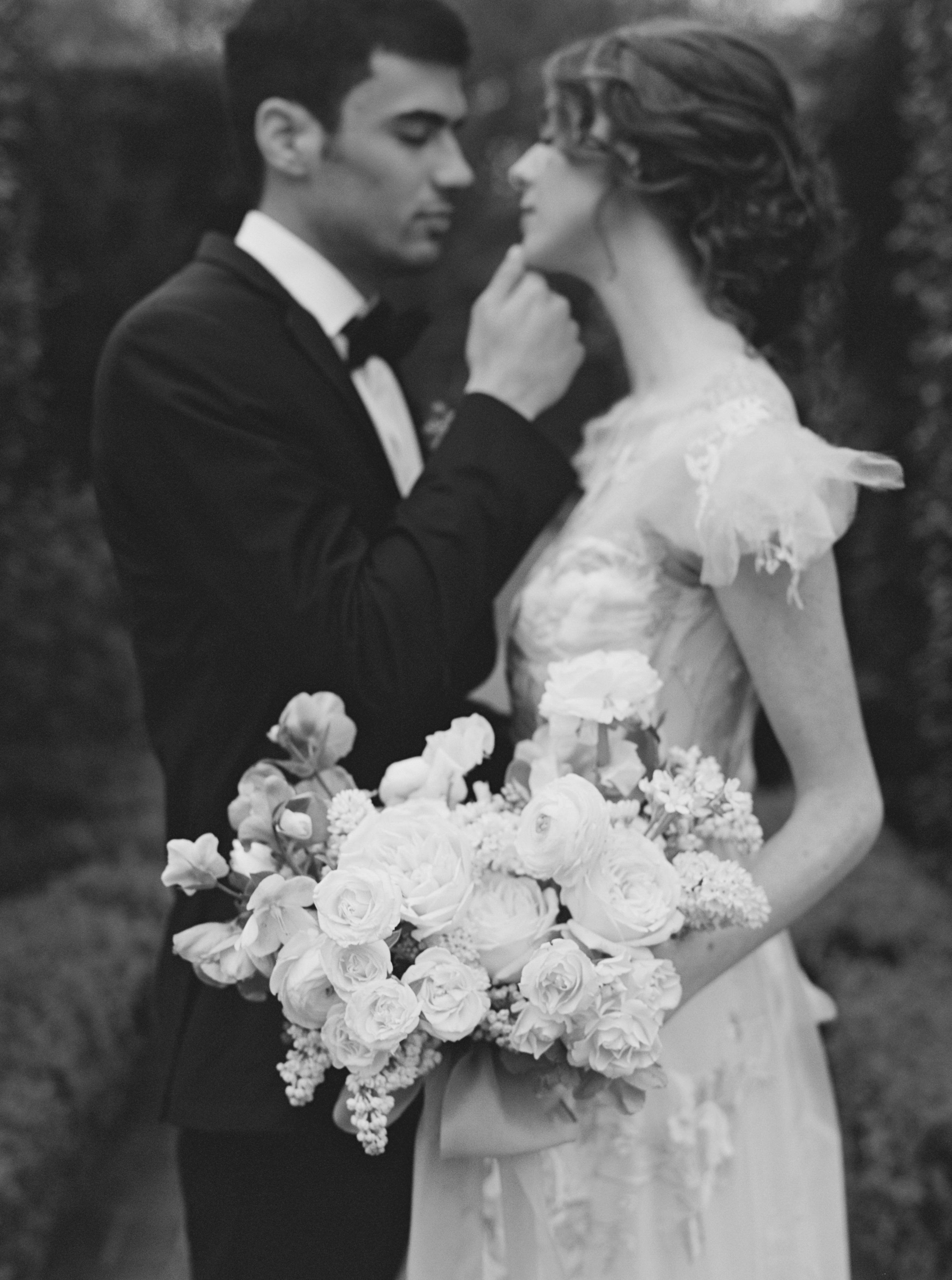 Black and white portrait of a bride and groom holding a lush bridal bouquet of garden roses and ranunculus.