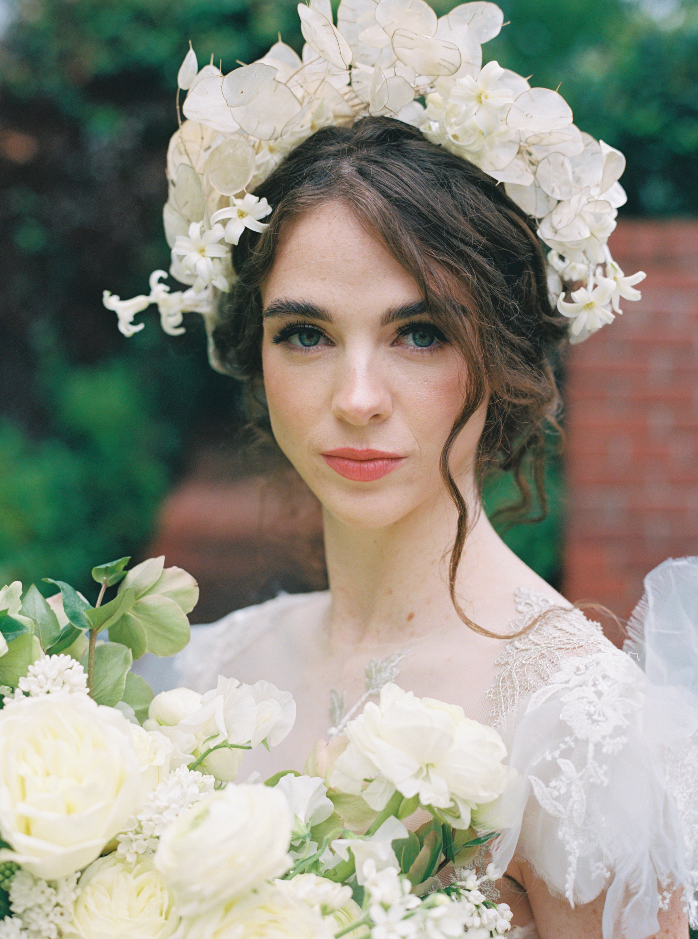 A bride wearing an ethereal floral crown of lunaria seed pods and white blossoms alongside a soft white bouquet.