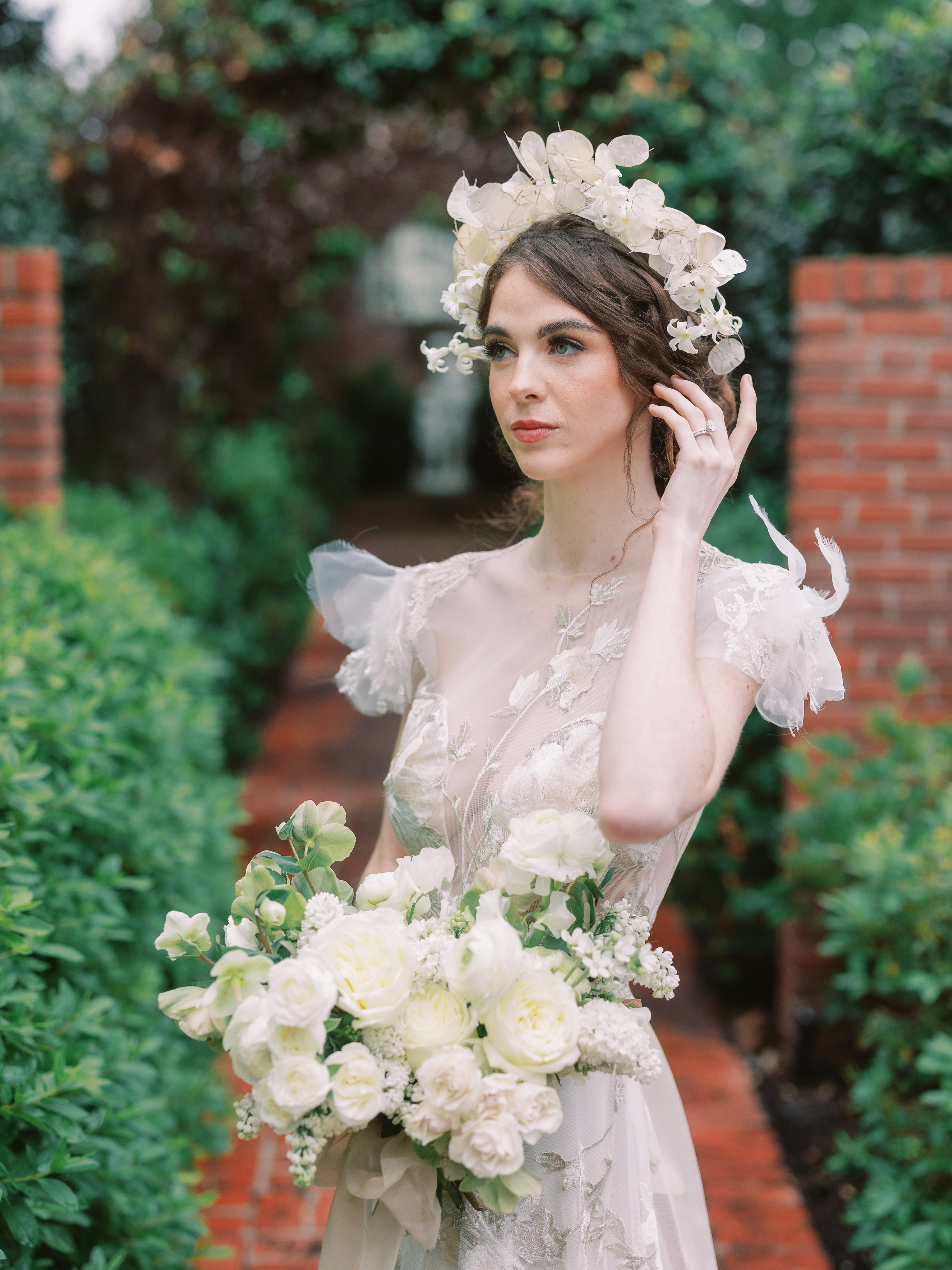 A bride in an embroidered gown wearing a delicate floral crown and holding a lush bouquet of white roses.