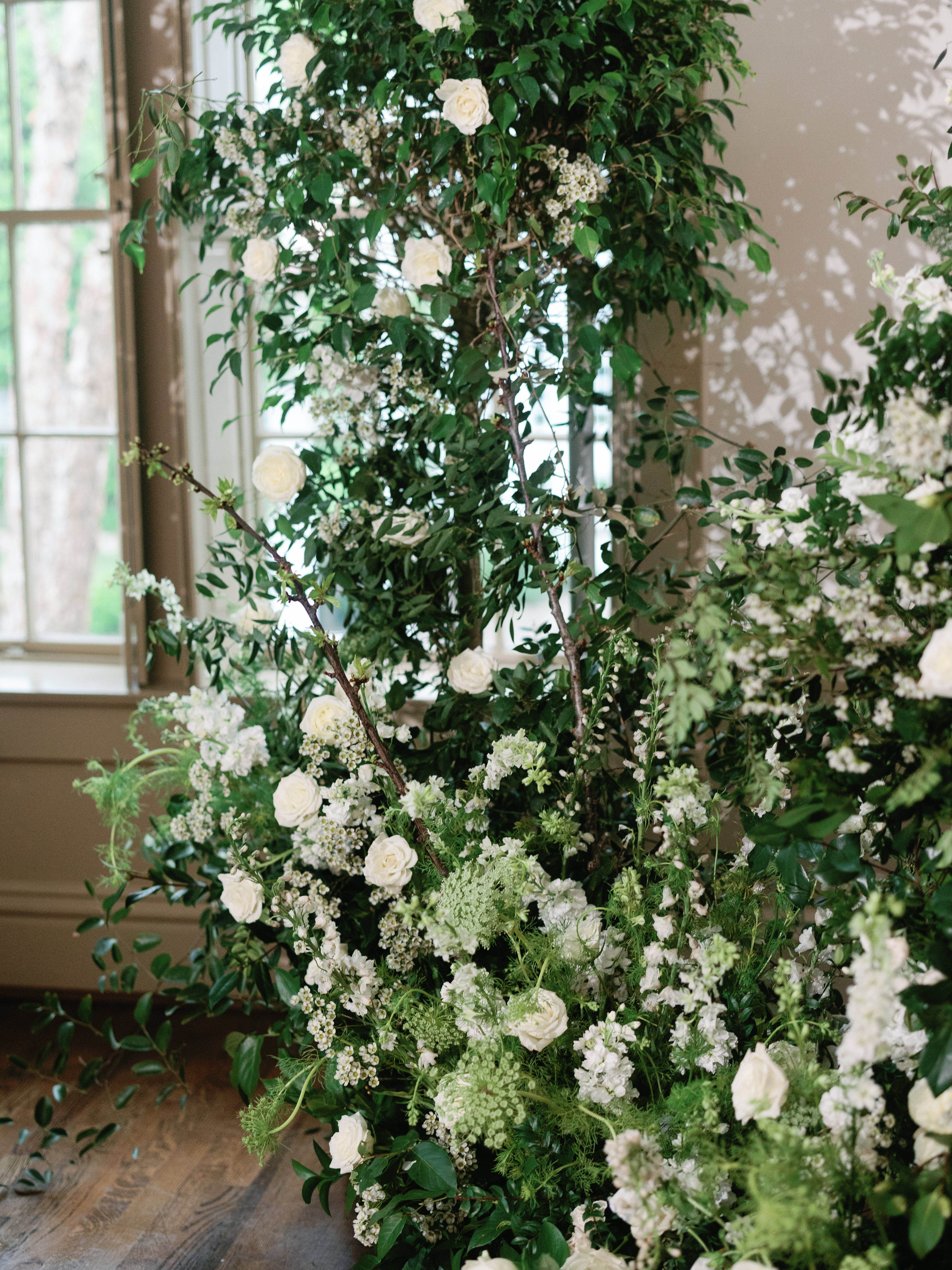 Lush floral installation featuring white roses, delicate wild blossoms, and abundant greenery entwined with natural branches.