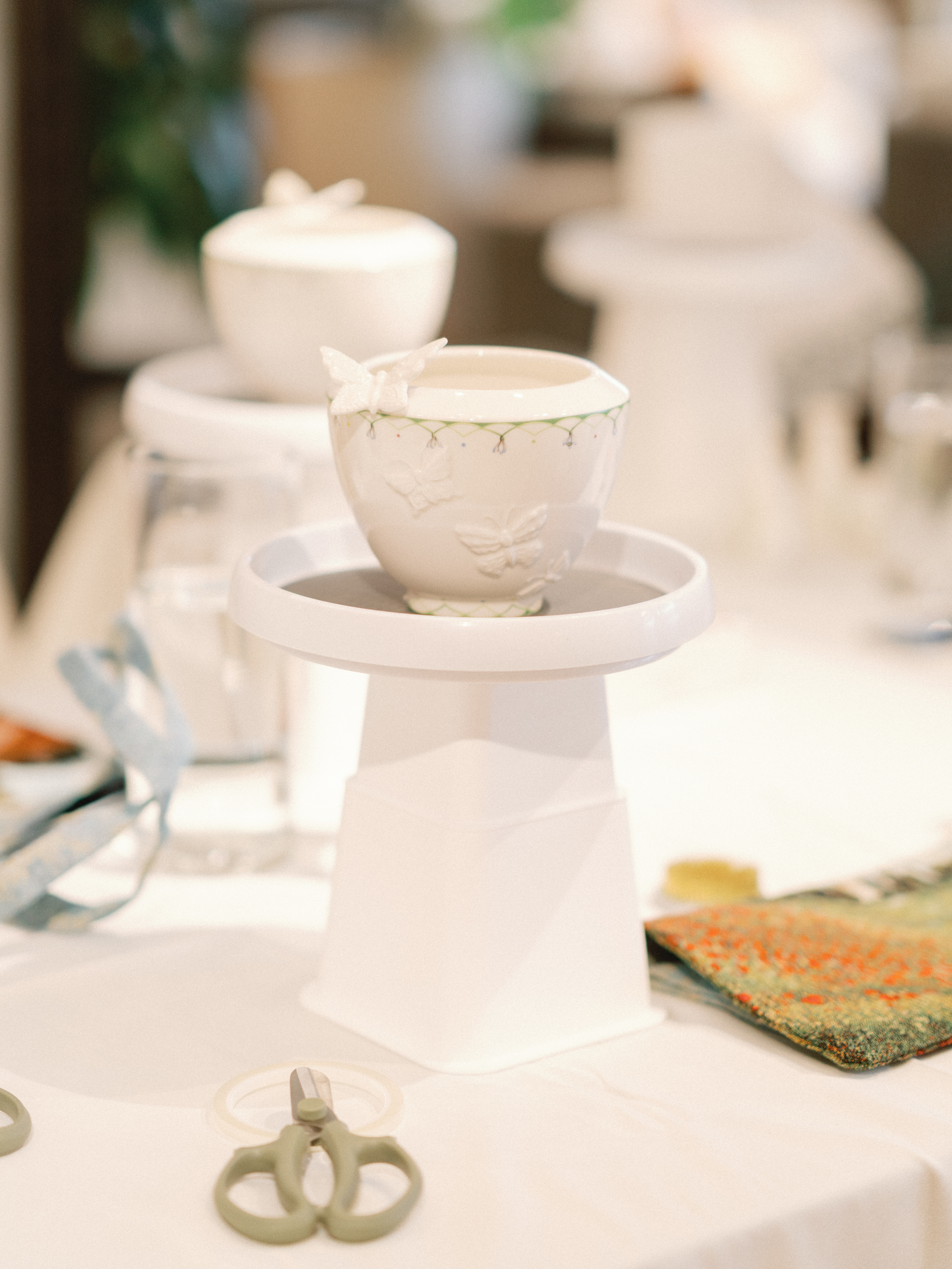 A white ceramic vessel adorned with raised butterfly motifs sits on a matching pedestal stand.