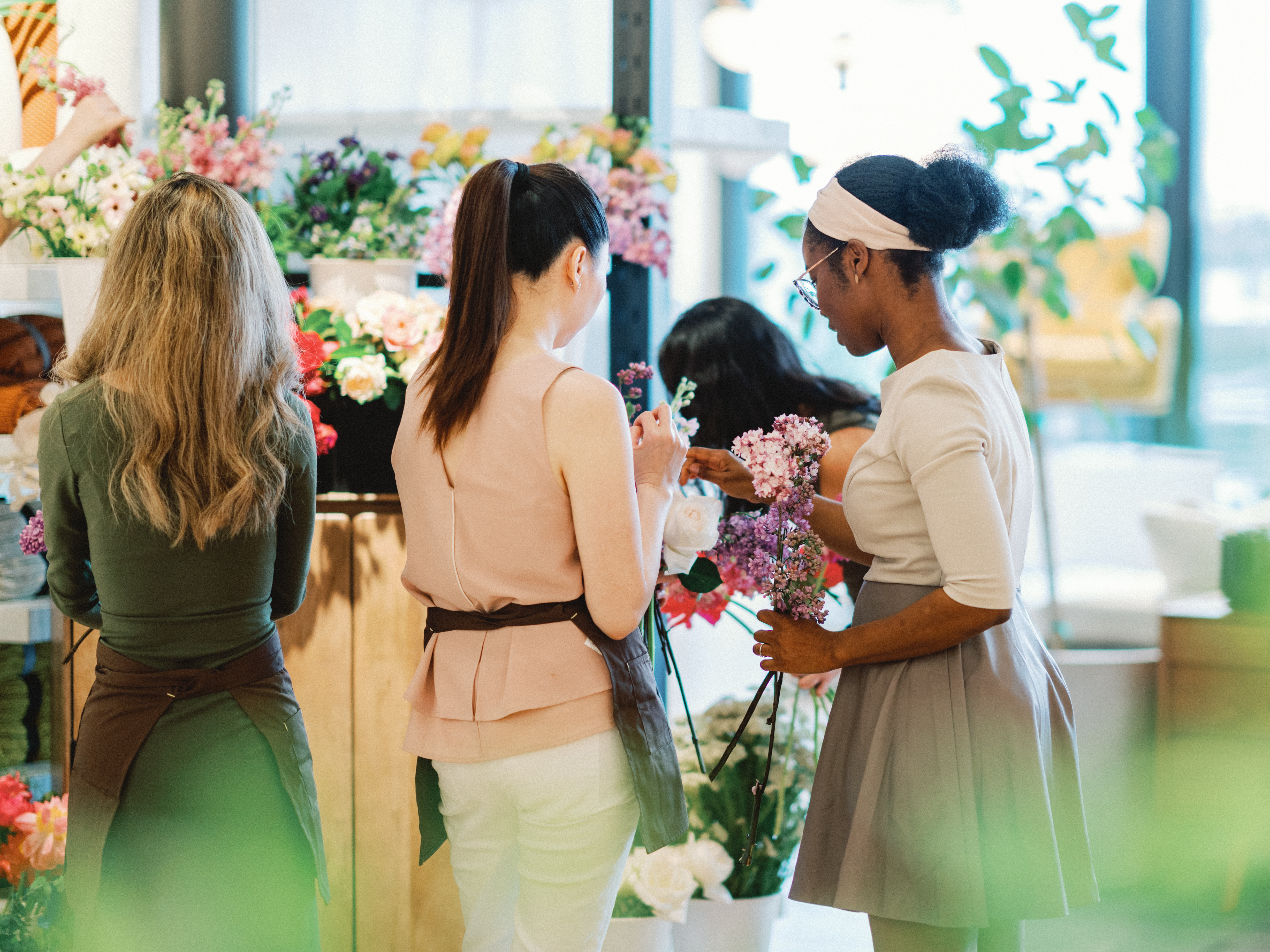 Participants arrange fresh white roses and purple lilacs during a hands-on floral design workshop.
