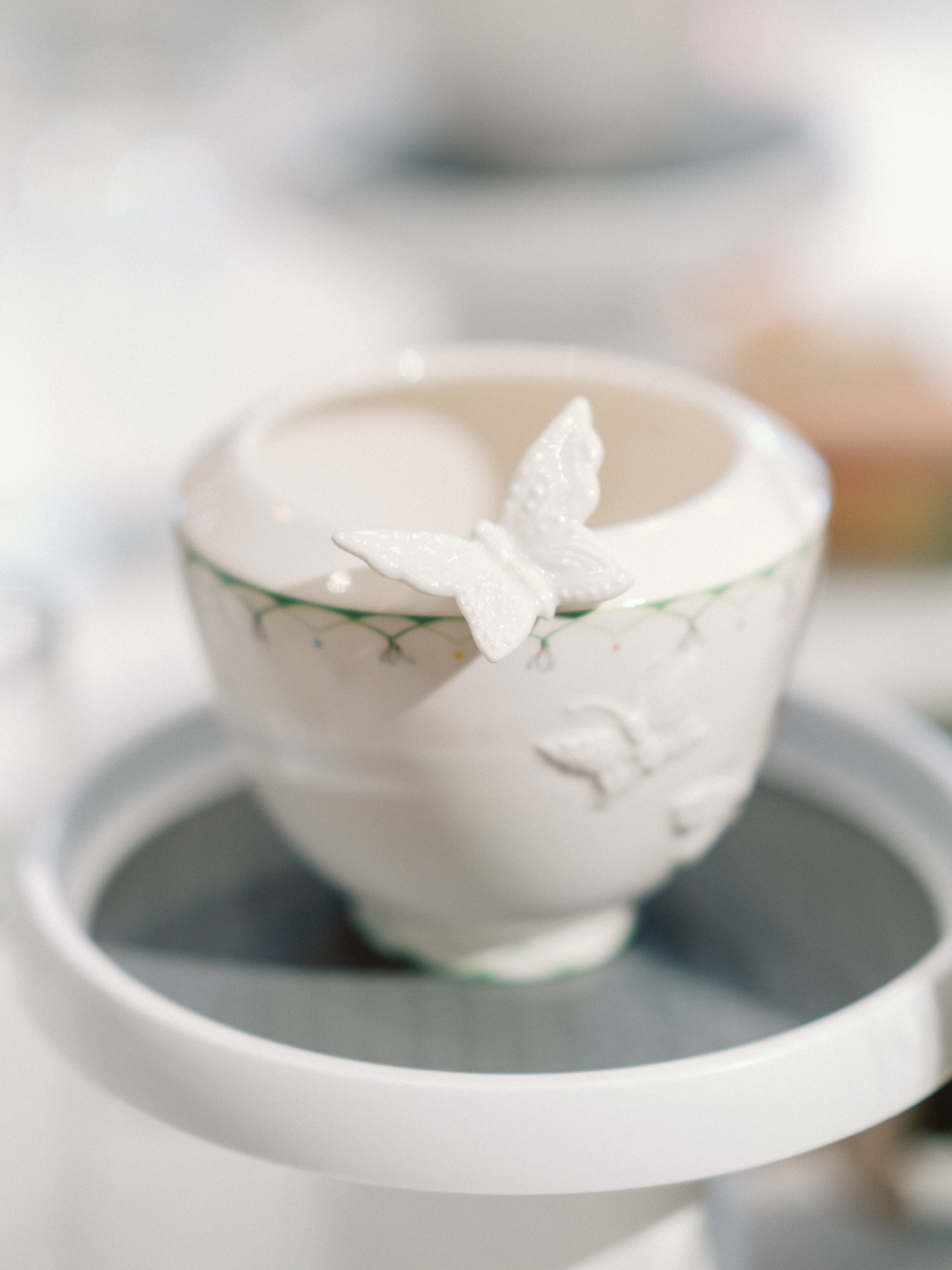 A close-up of a white ceramic cup adorned with a delicate sculpted butterfly along the rim.