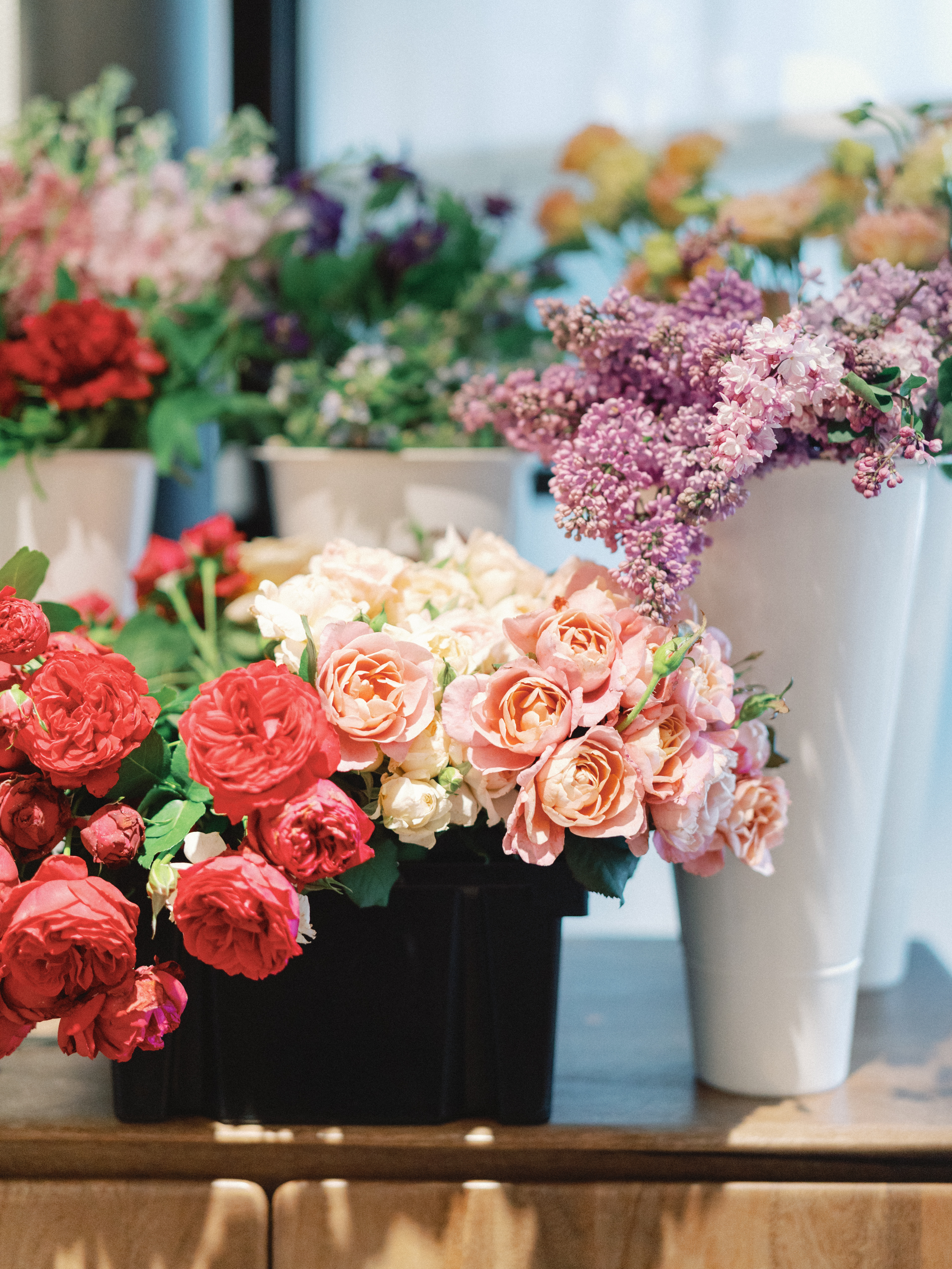 Clusters of fresh peach garden roses and miniature white roses arranged near blooming lilac stems.