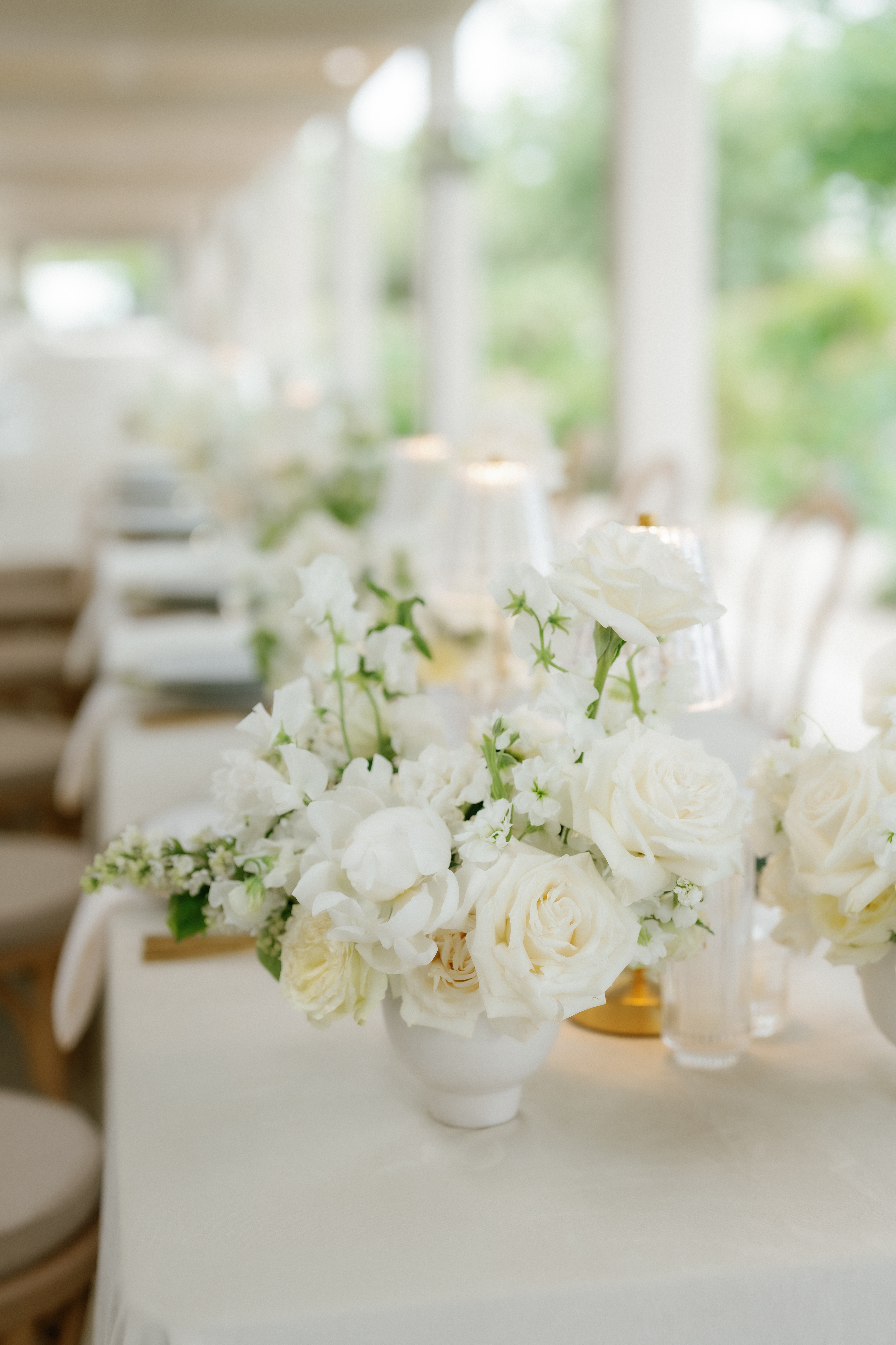 White roses and sweet peas arranged in a low ceramic bowl on a softly lit reception table.
