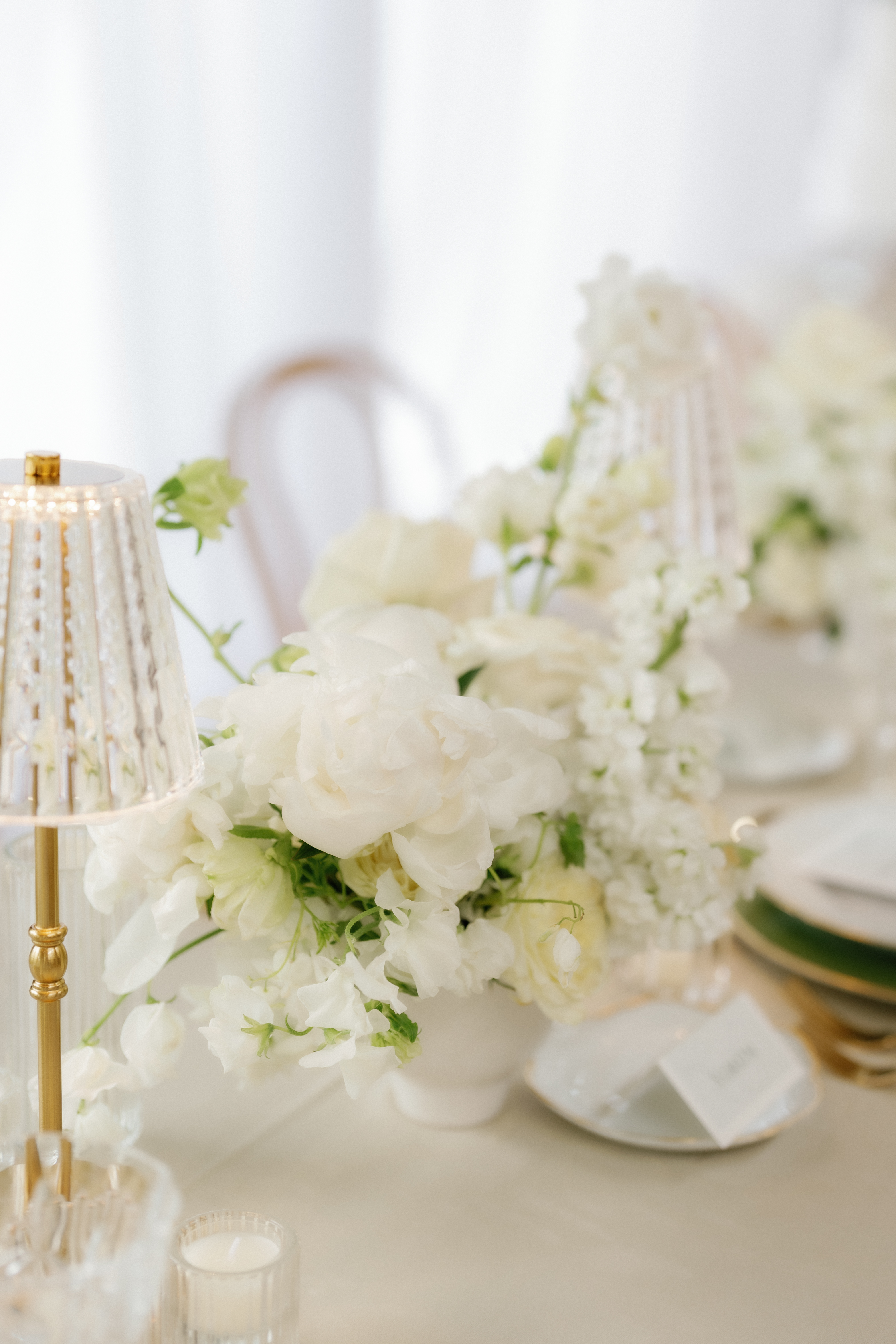Close-up of a delicate white floral centerpiece featuring sweet peas and soft ruffled blossoms on a reception table.