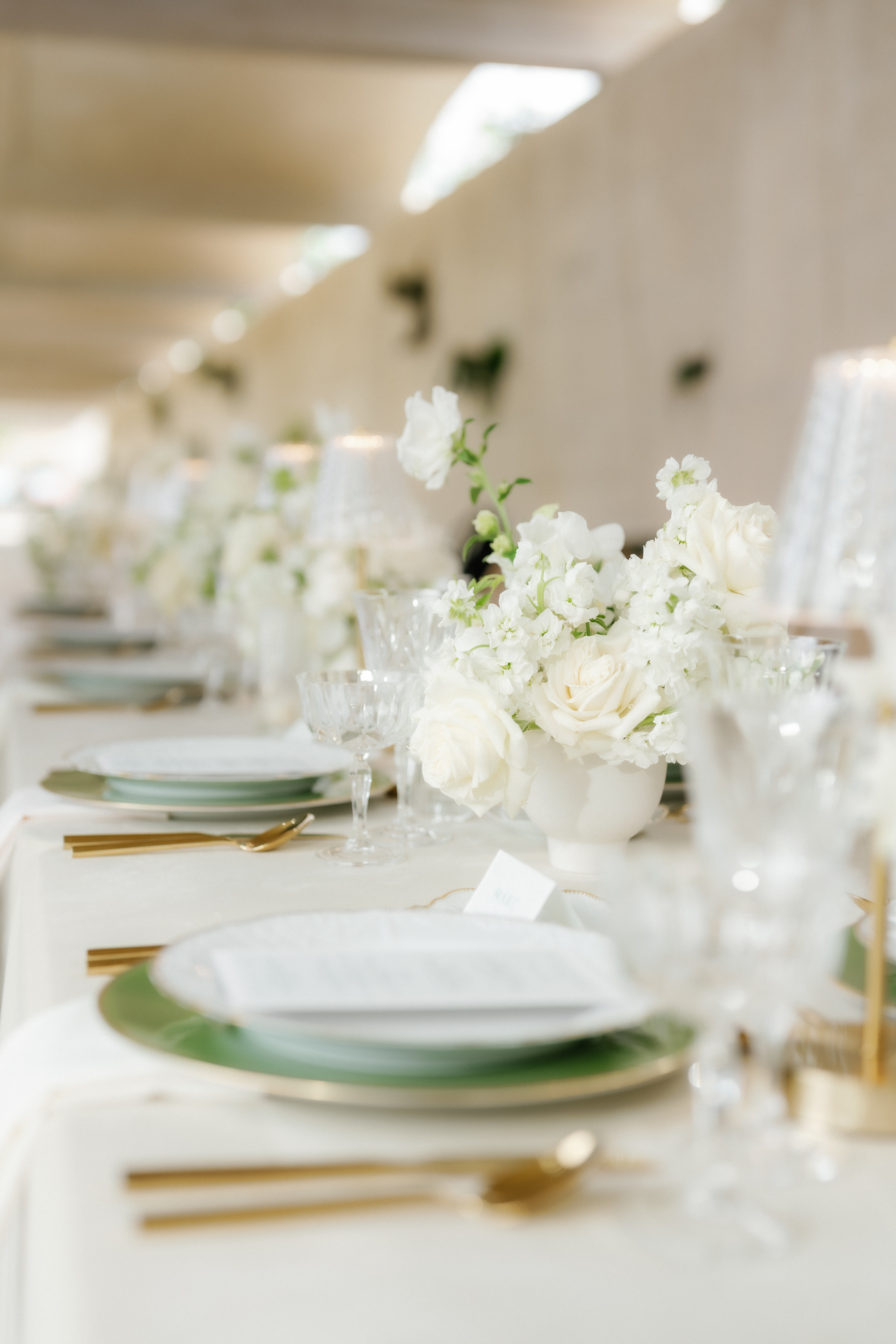 White roses and delicate blooms beside cut crystal glassware on an elegant wedding reception table.