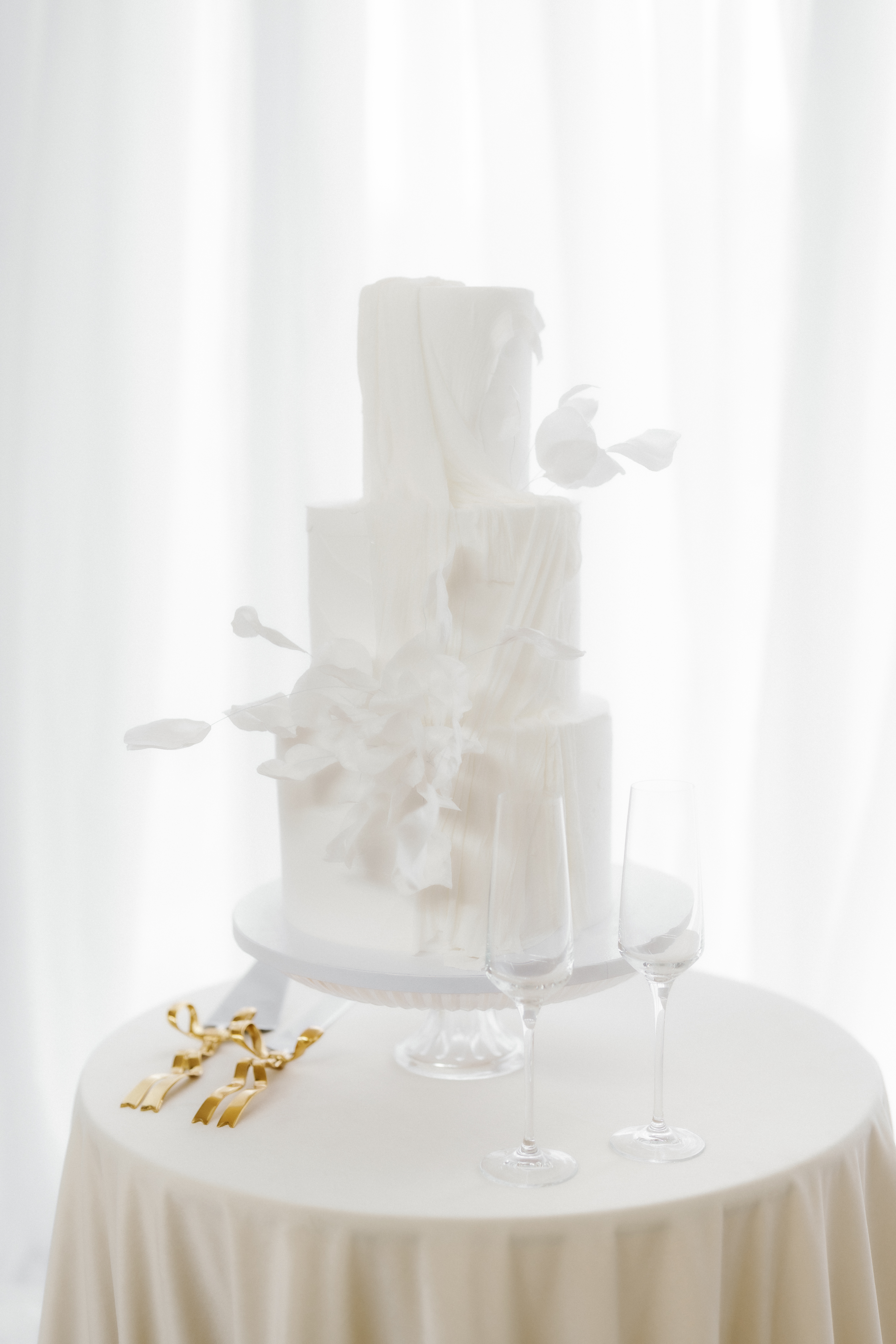 Textured white tiered wedding cake with delicate sculptural details displayed beside a champagne flute.