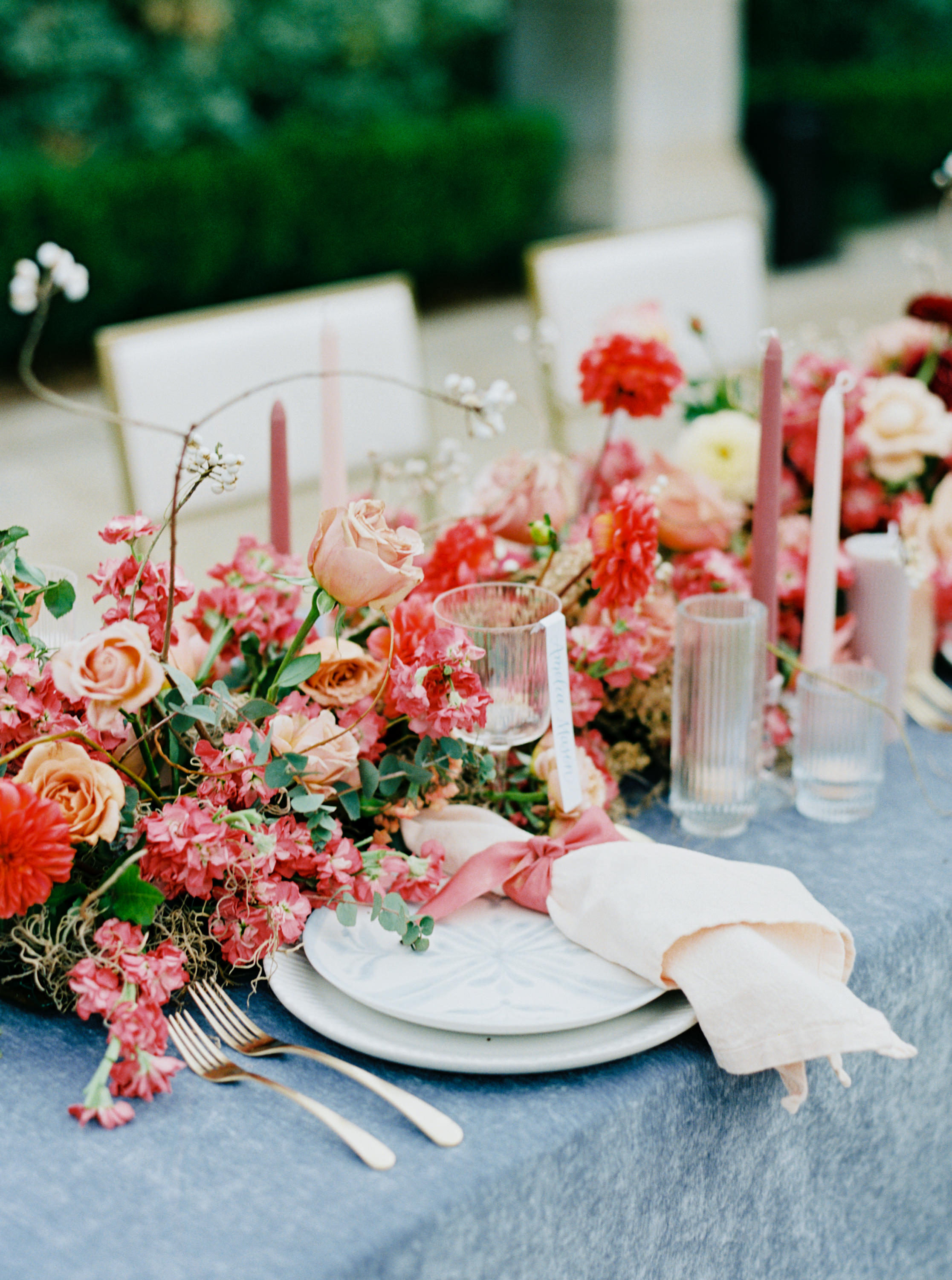 A romantic wedding table setting featuring lush pink and coral floral arrangements, fluted glassware, and patterned dinnerware.