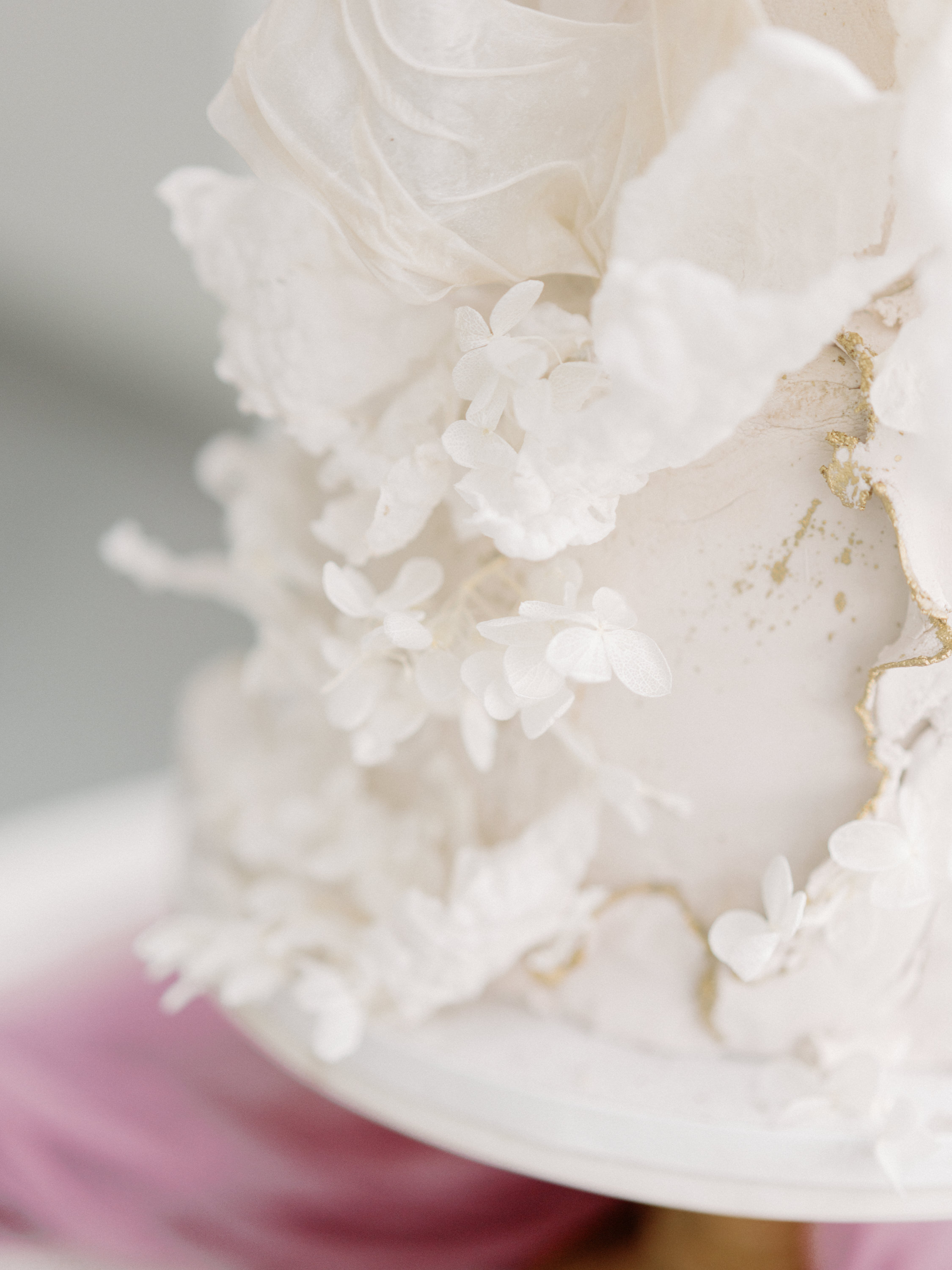 Close-up detail of a white wedding cake adorned with delicate white hydrangea florets and soft textured petals.