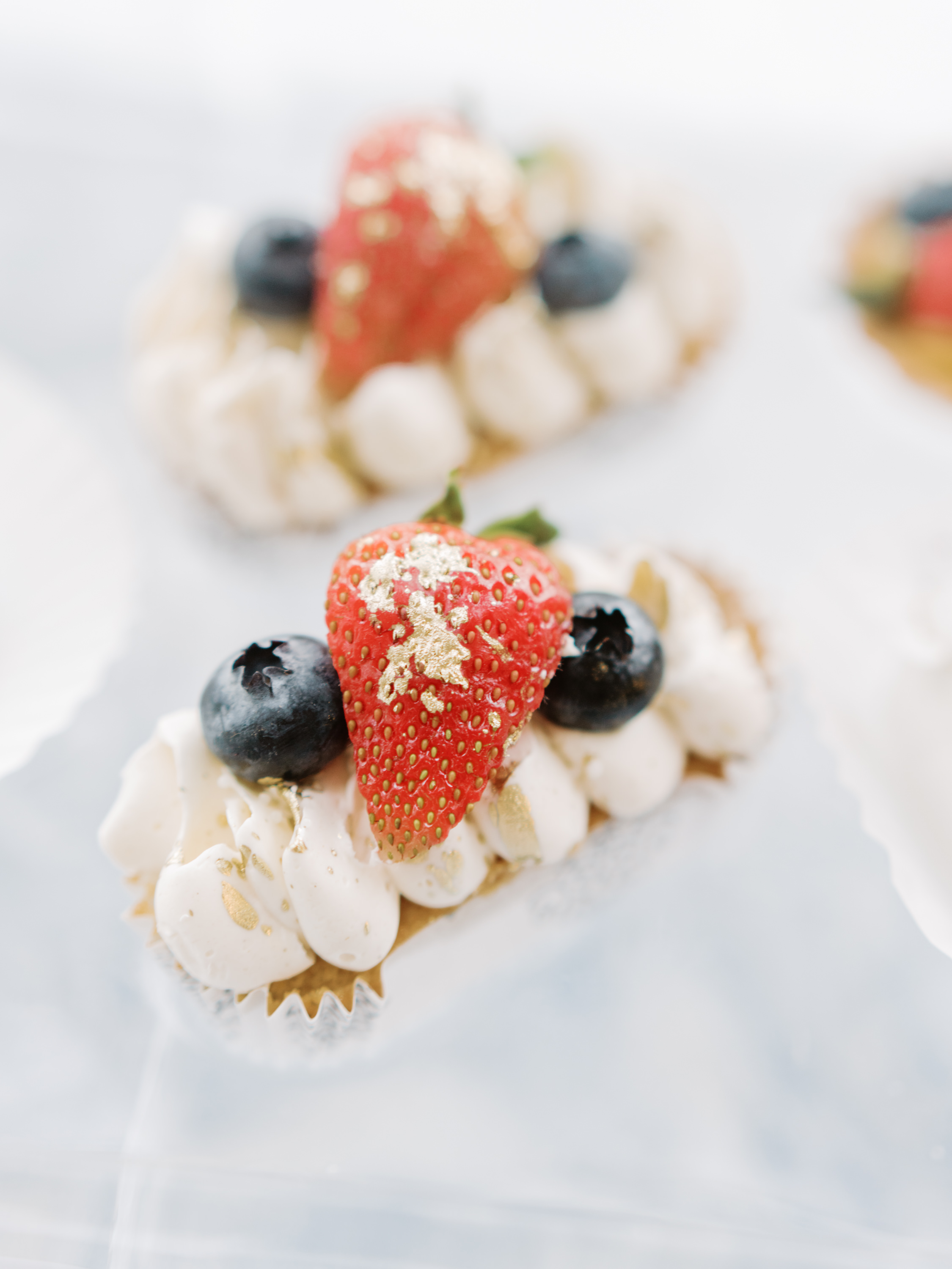 Individual berry pastries garnished with fresh strawberries, blueberries, and edible gold leaf.