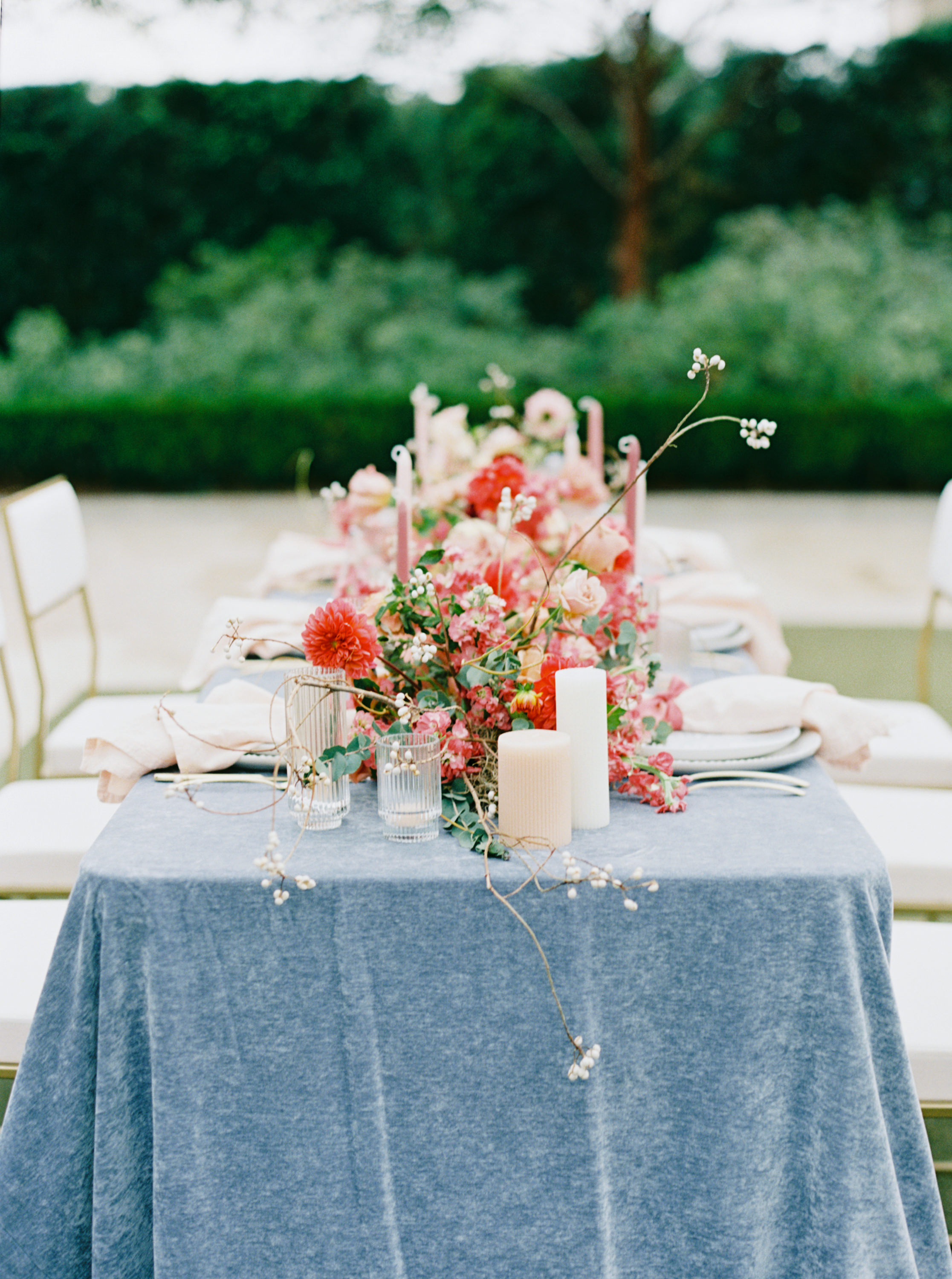 A wedding dining table styled with a slate blue tablecloth, vibrant pink and coral floral arrangements, and romantic candlelight.