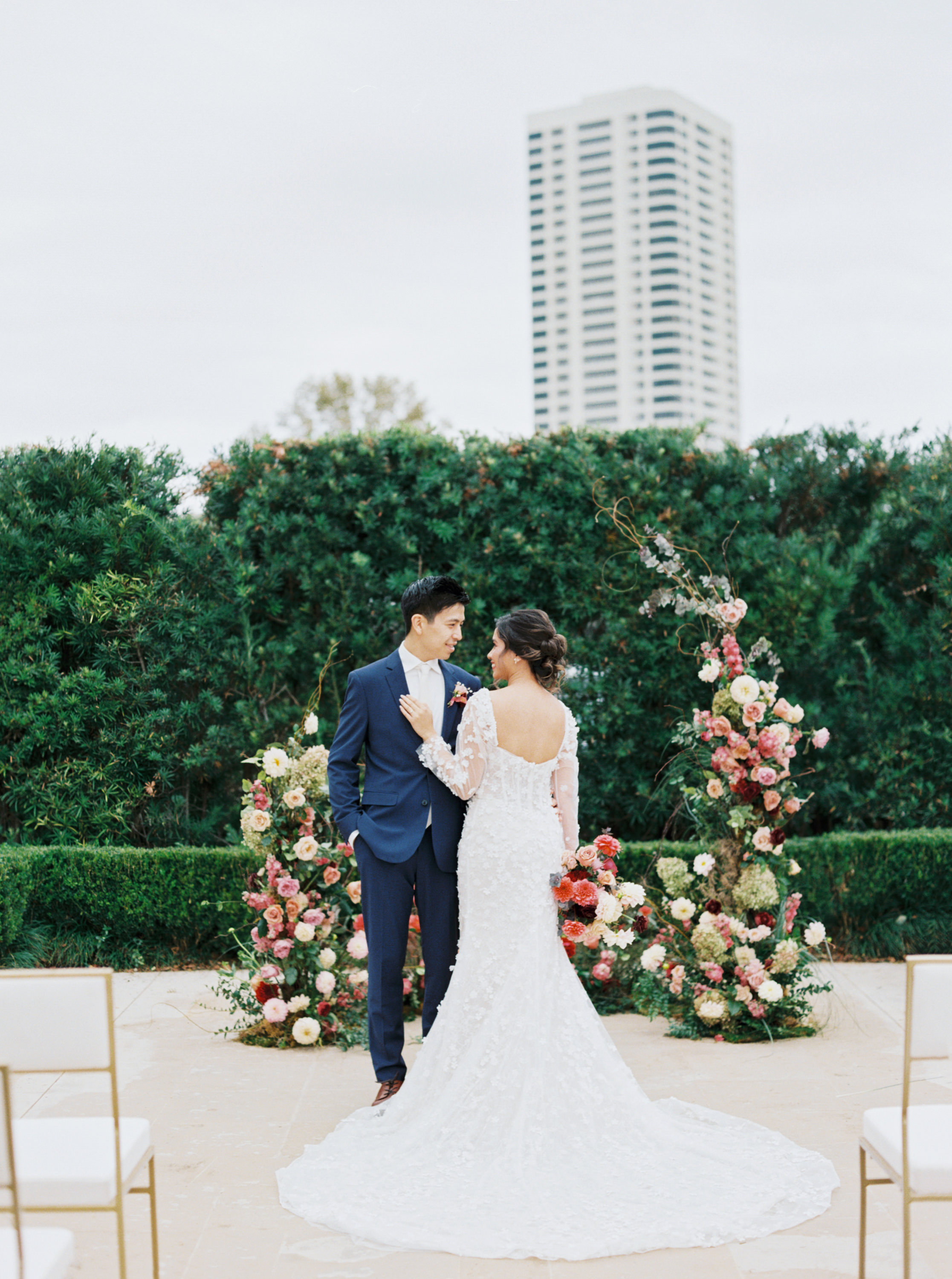 Bride and groom standing together before an organic floral ceremony installation with pink and blush blooms.