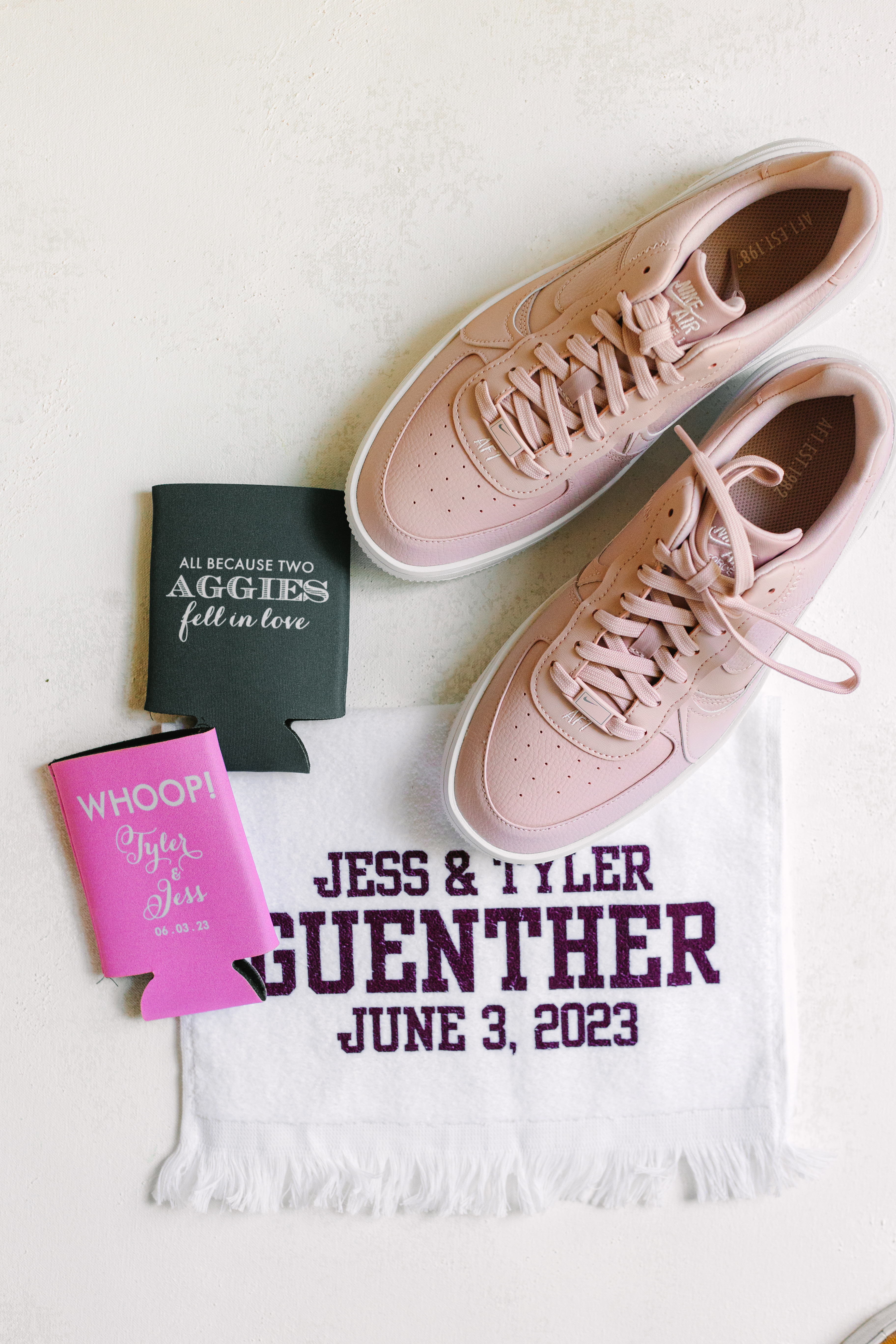 Blush pink sneakers arranged beside a personalized white towel and dark drink cooler.