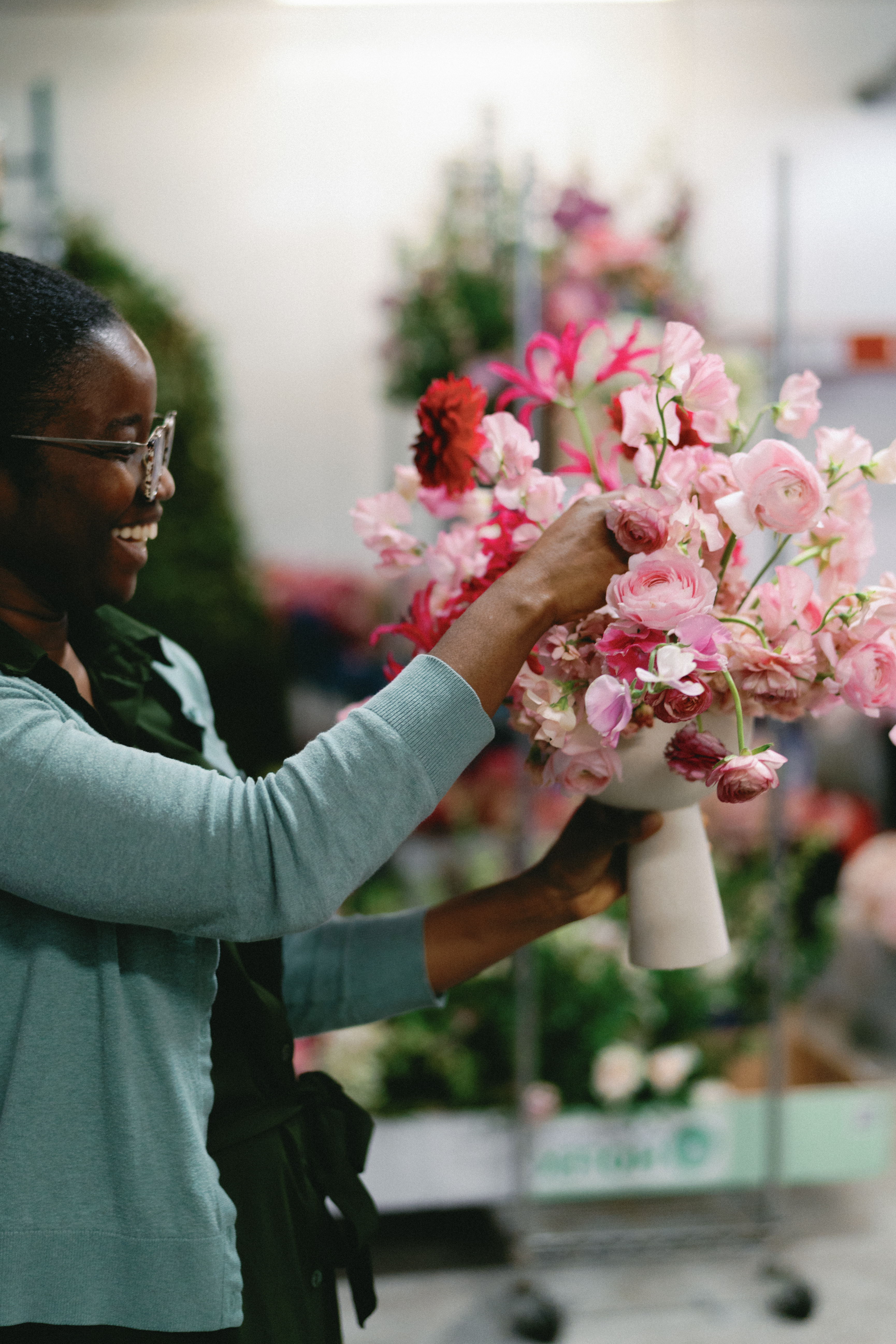 Hands carefully arrange vibrant pink sweet peas and deep red blossoms in a floral studio.