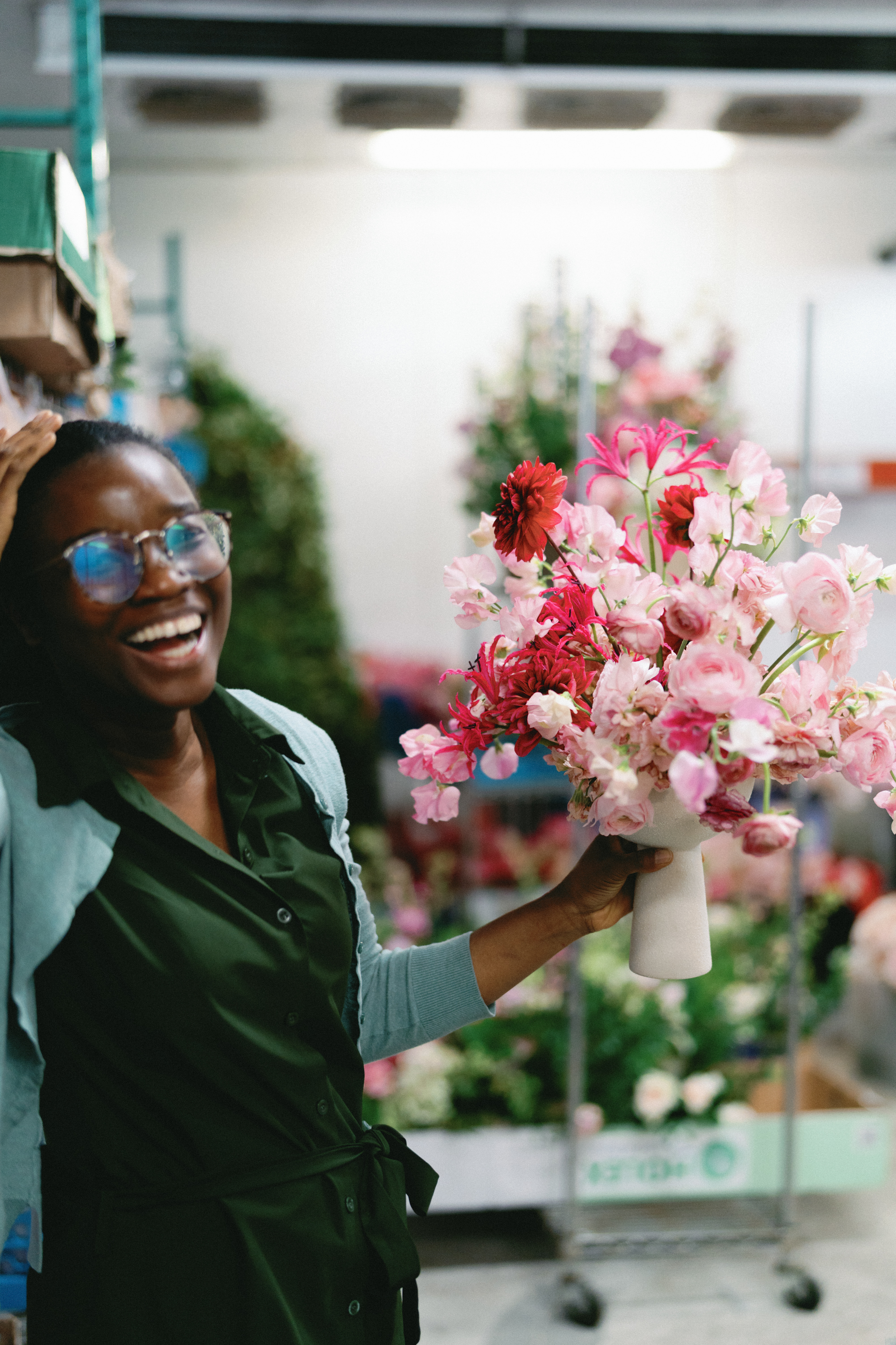 A florist wearing a green apron holds a vibrant bouquet of pink sweet peas and deep red blossoms in a studio.