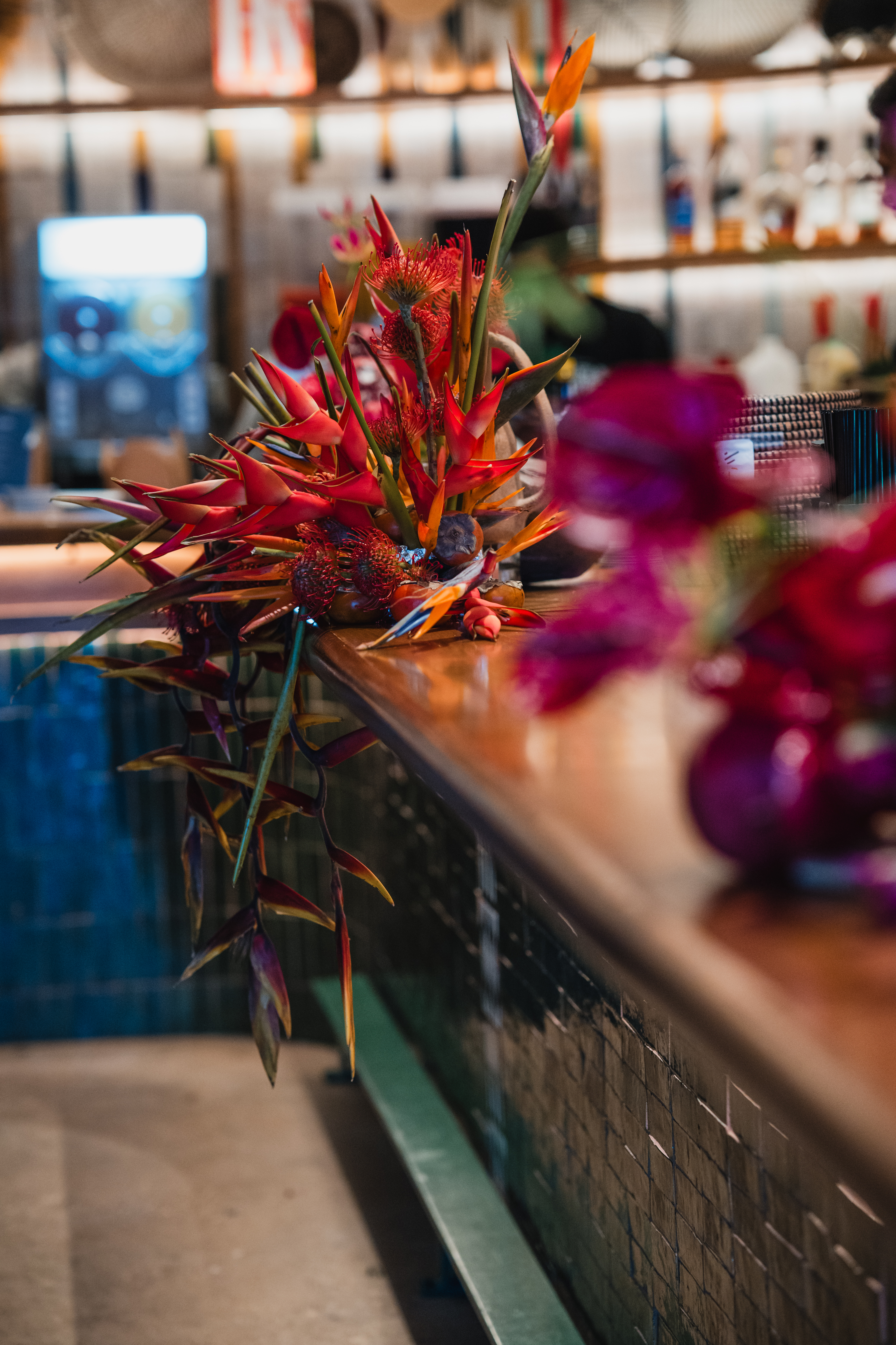A vibrant tropical floral arrangement featuring birds of paradise and pincushion proteas on a polished wood counter.