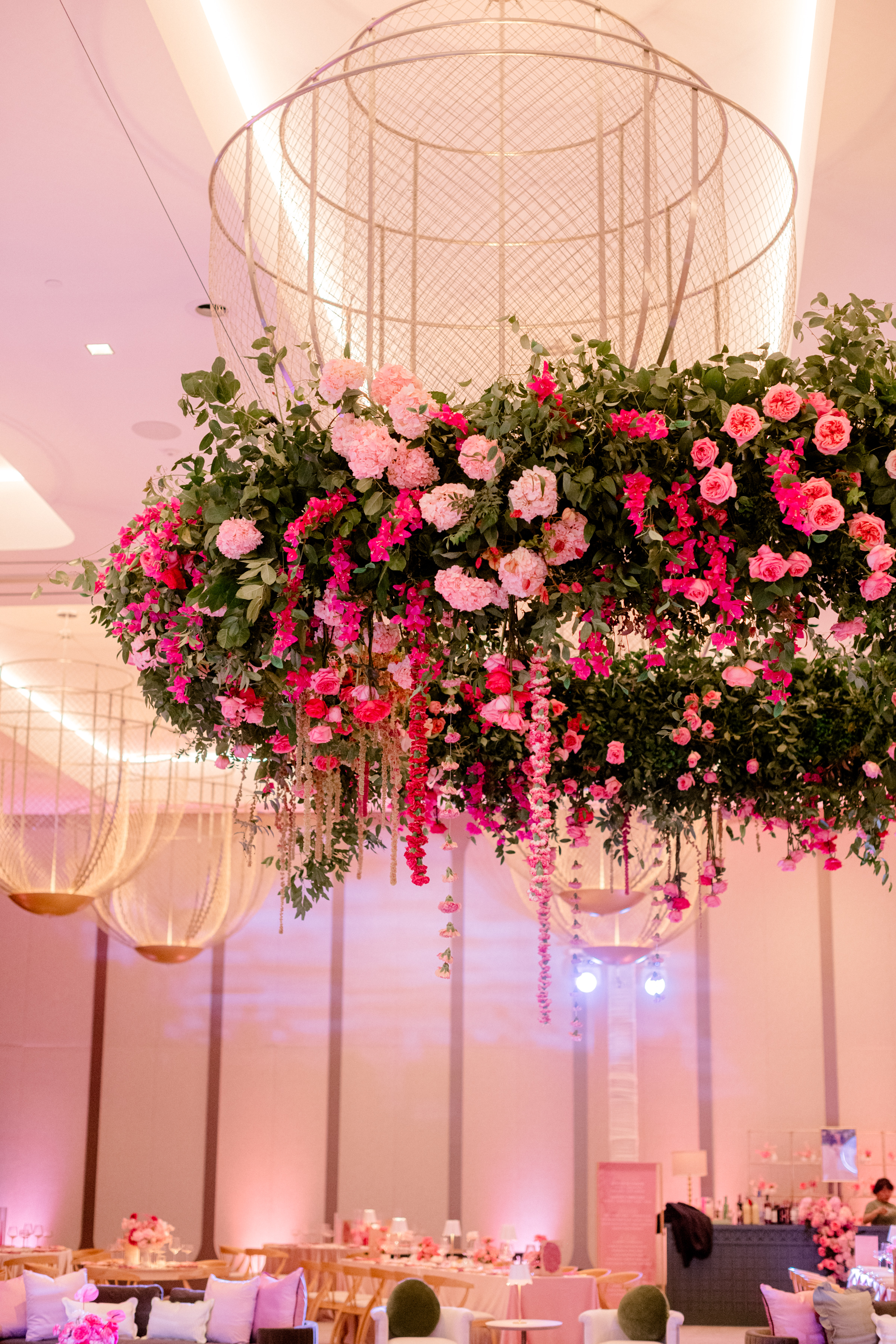 Hanging floral installation with pink hydrangeas, trailing blossoms, and greenery beneath an architectural wire structure.