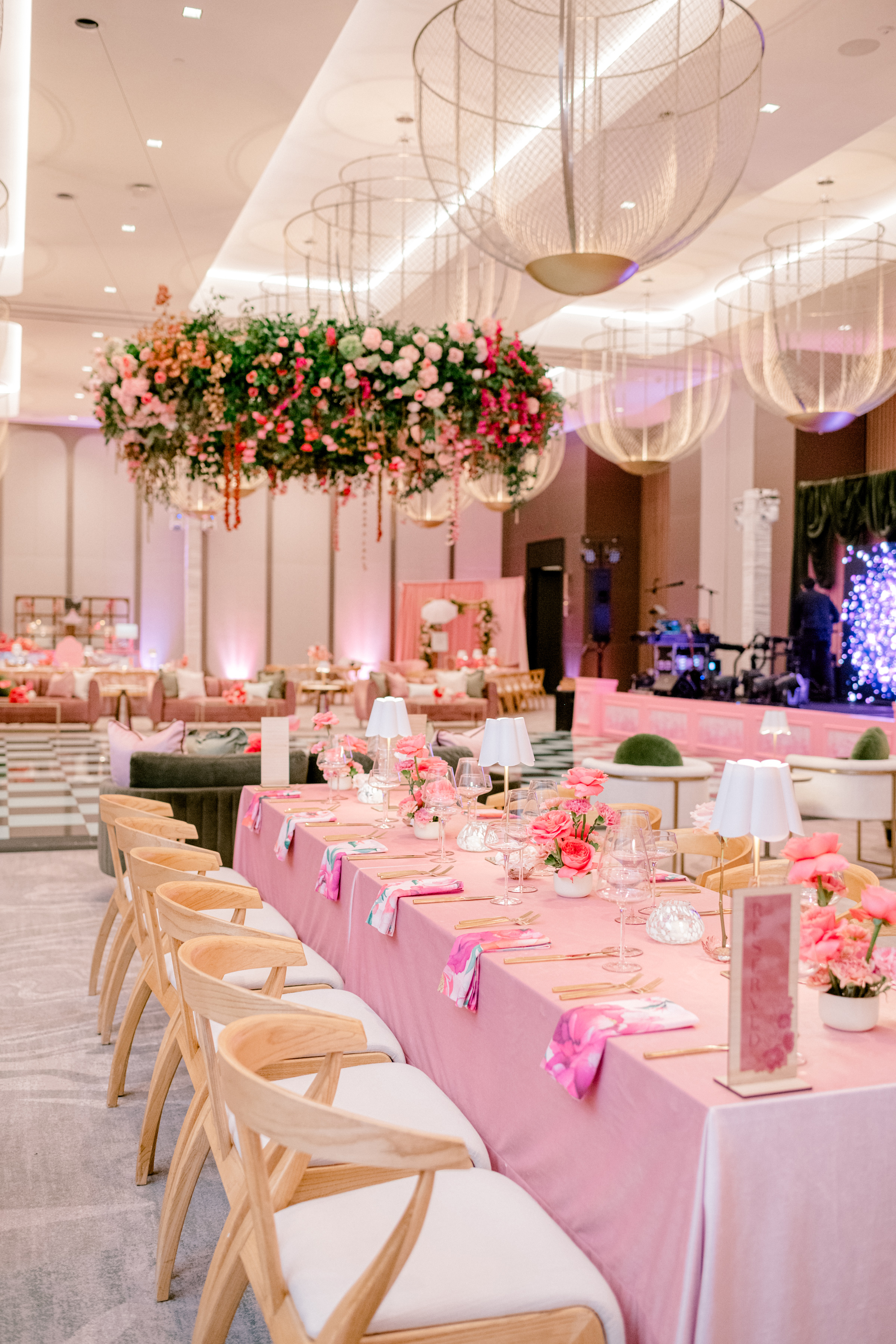 Pink celebration tablescape styled with rose centerpieces beneath an expansive suspended floral chandelier.