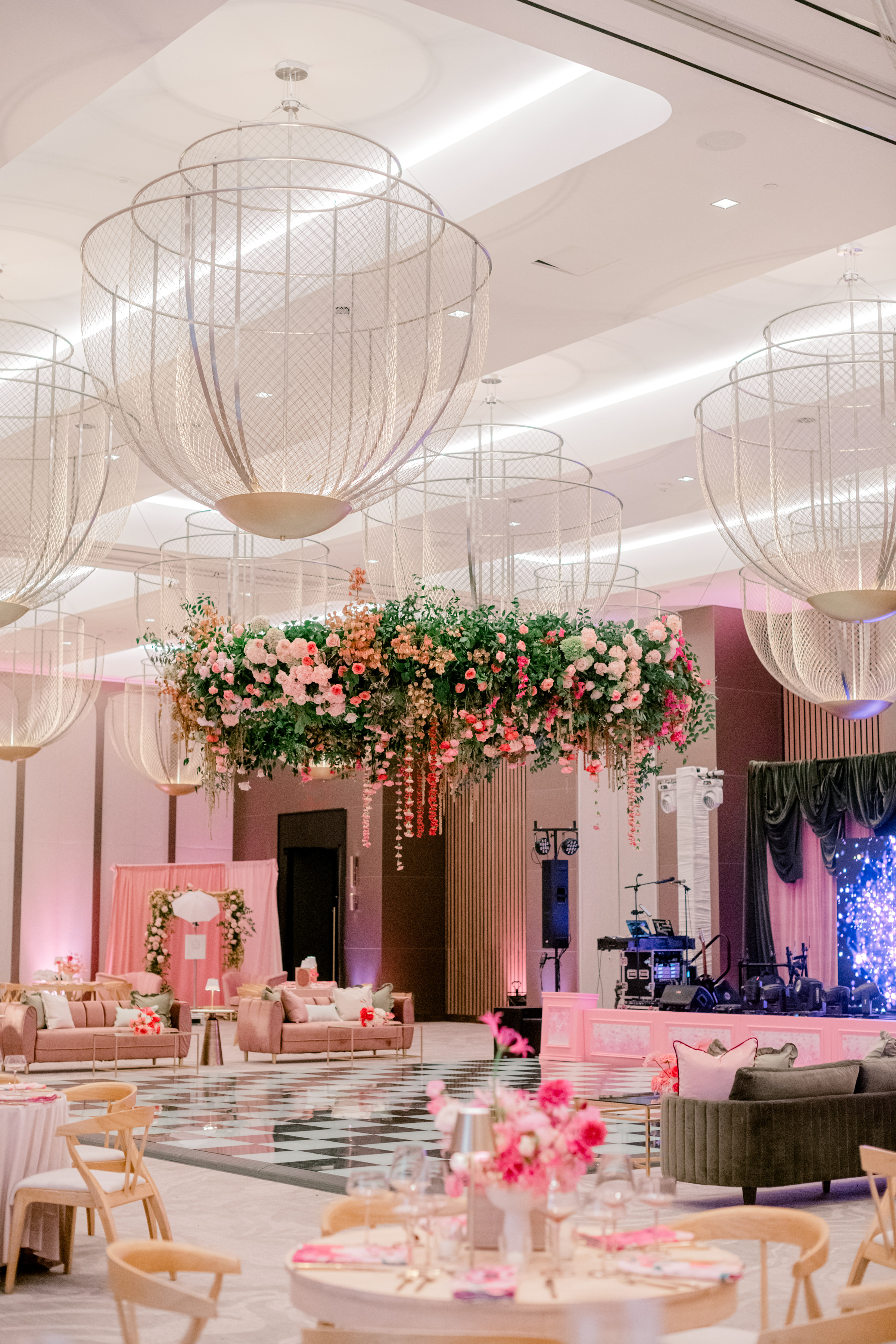 A lush suspended floral installation of pink roses hangs above a checkered dance floor and elegant lounge seating.