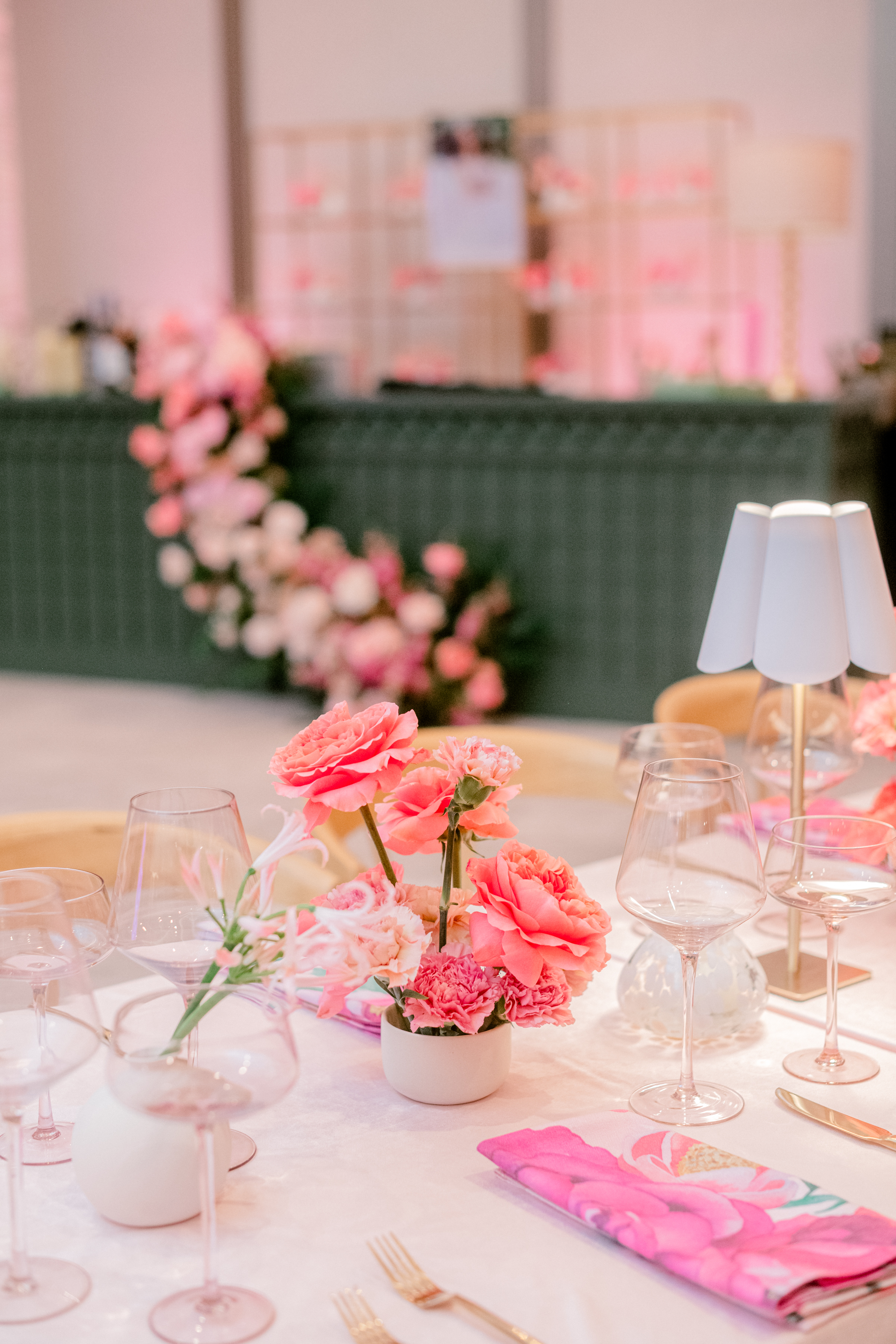A small centerpiece of coral roses and pink carnations on a dining table set with gold flatware and glassware.