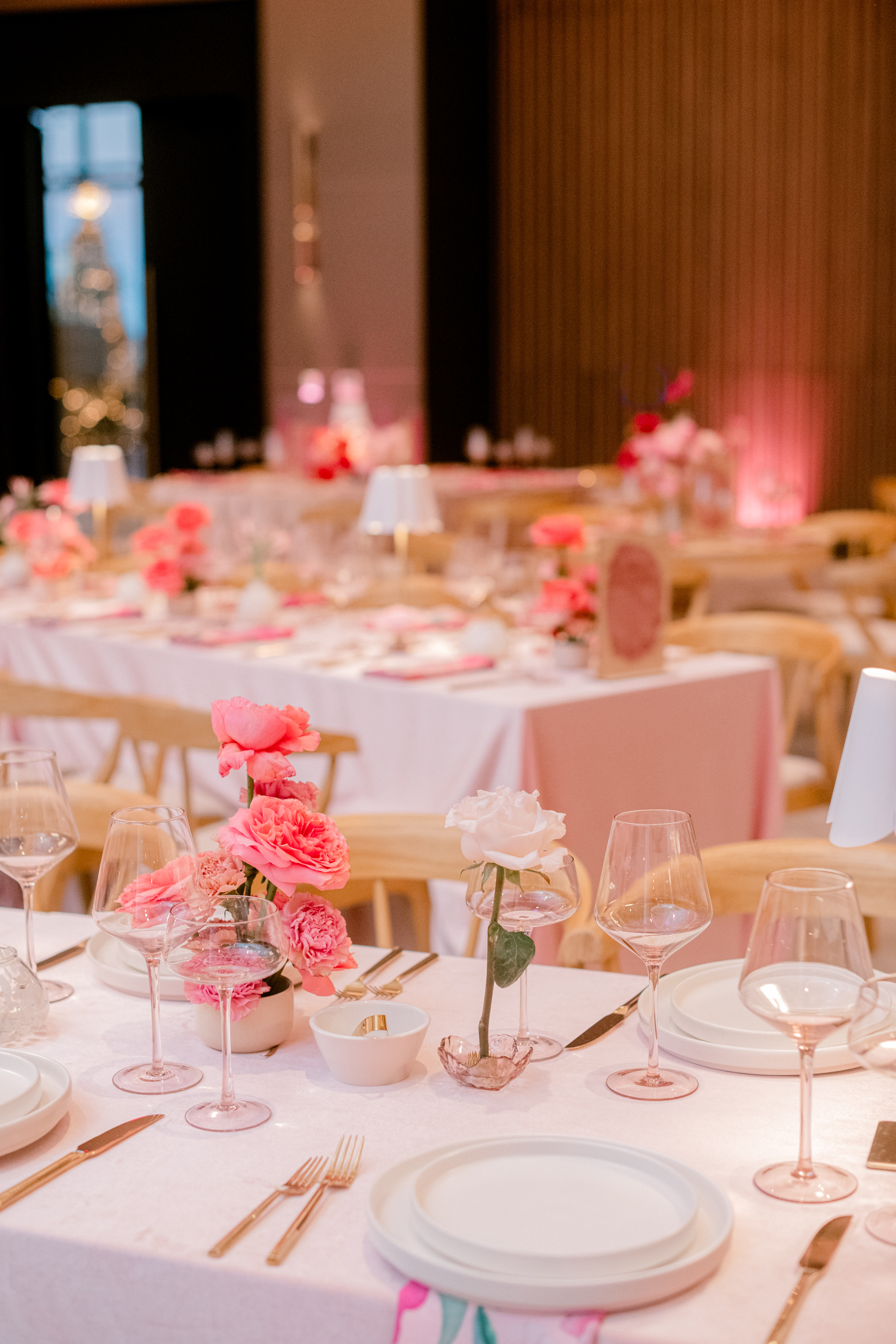 Pink and white dinner tablescape featuring delicate rose arrangements, modern glassware, and gold cutlery.