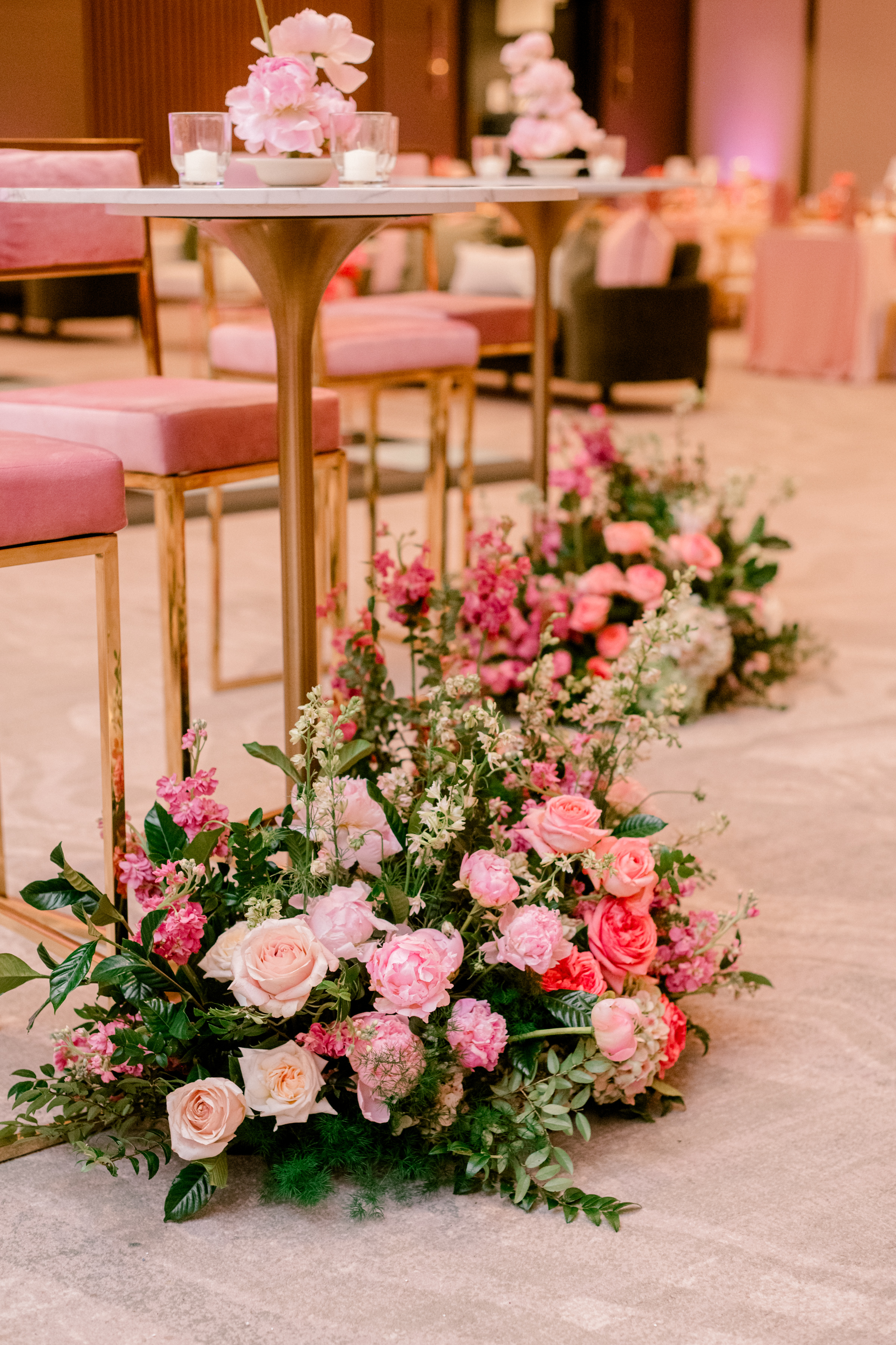 Lush ground floral meadow of pink peonies and roses beneath modern gold cocktail tables and velvet seating.