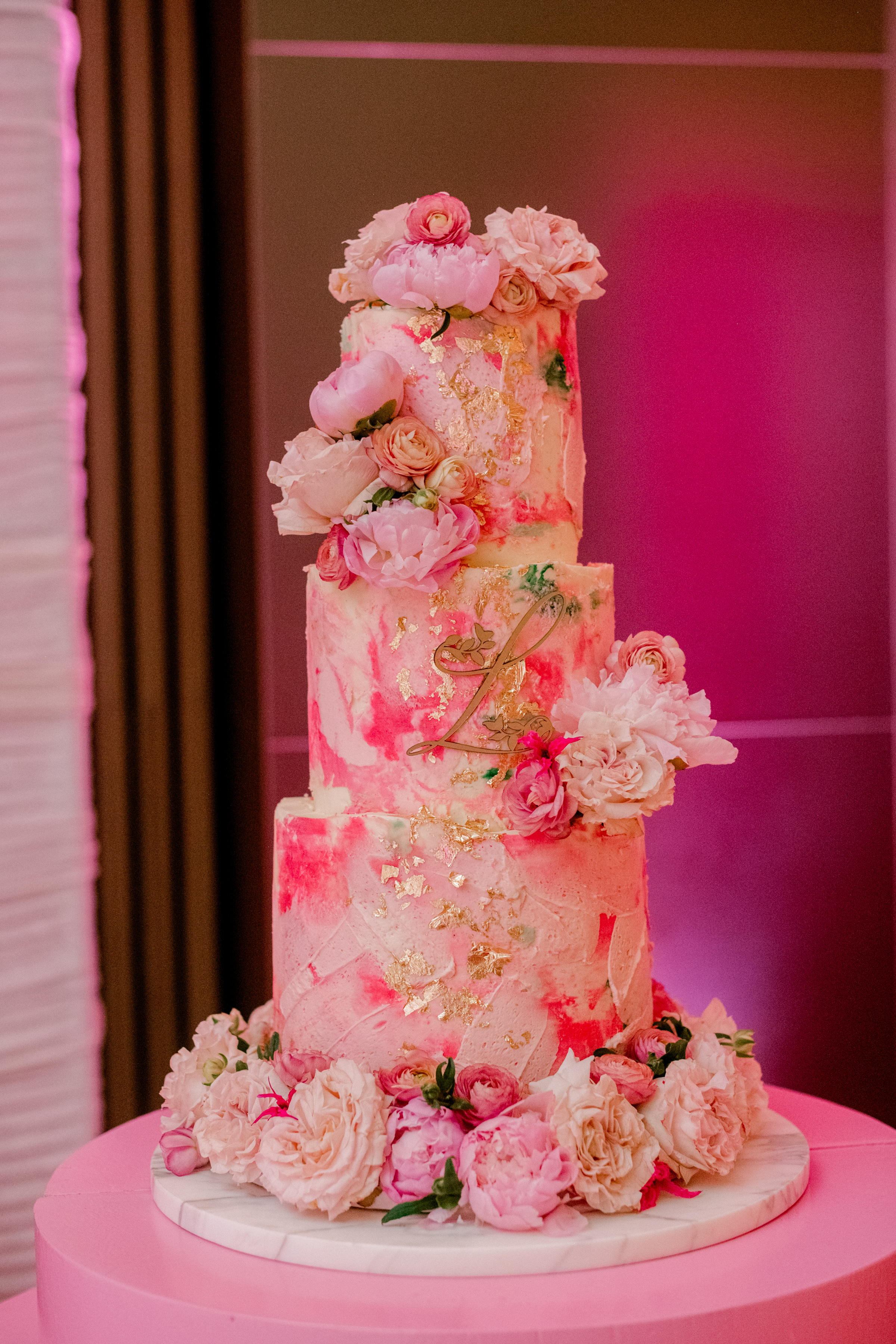 A three-tier pink marble cake accented with gold leaf flakes and fresh pink peonies and roses.