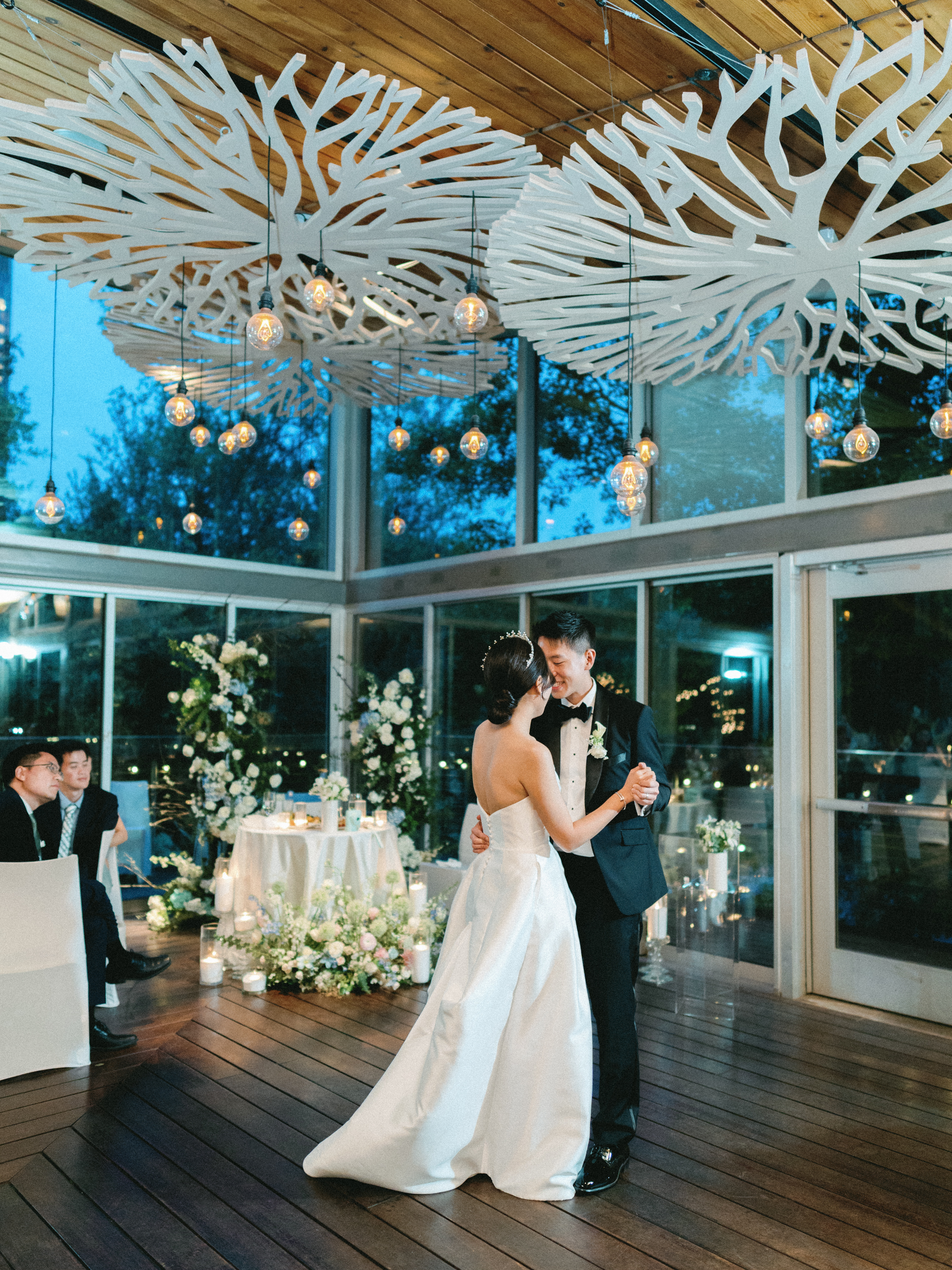 A bride and groom share a dance beneath hanging Edison bulbs and sculptural white ceiling installations.