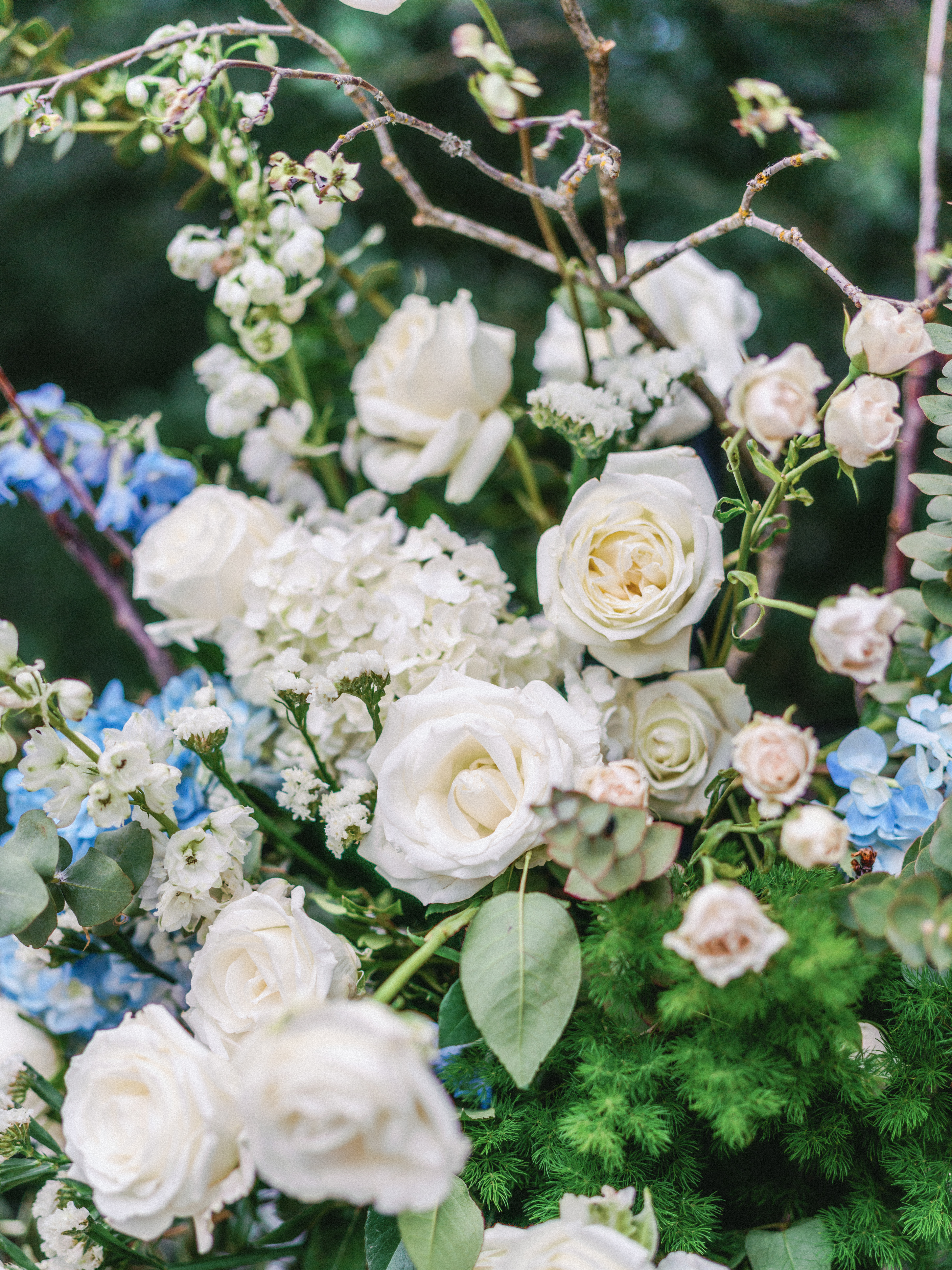 Close-up of elegant white roses and delicate hydrangeas woven with natural branches and lush greenery.